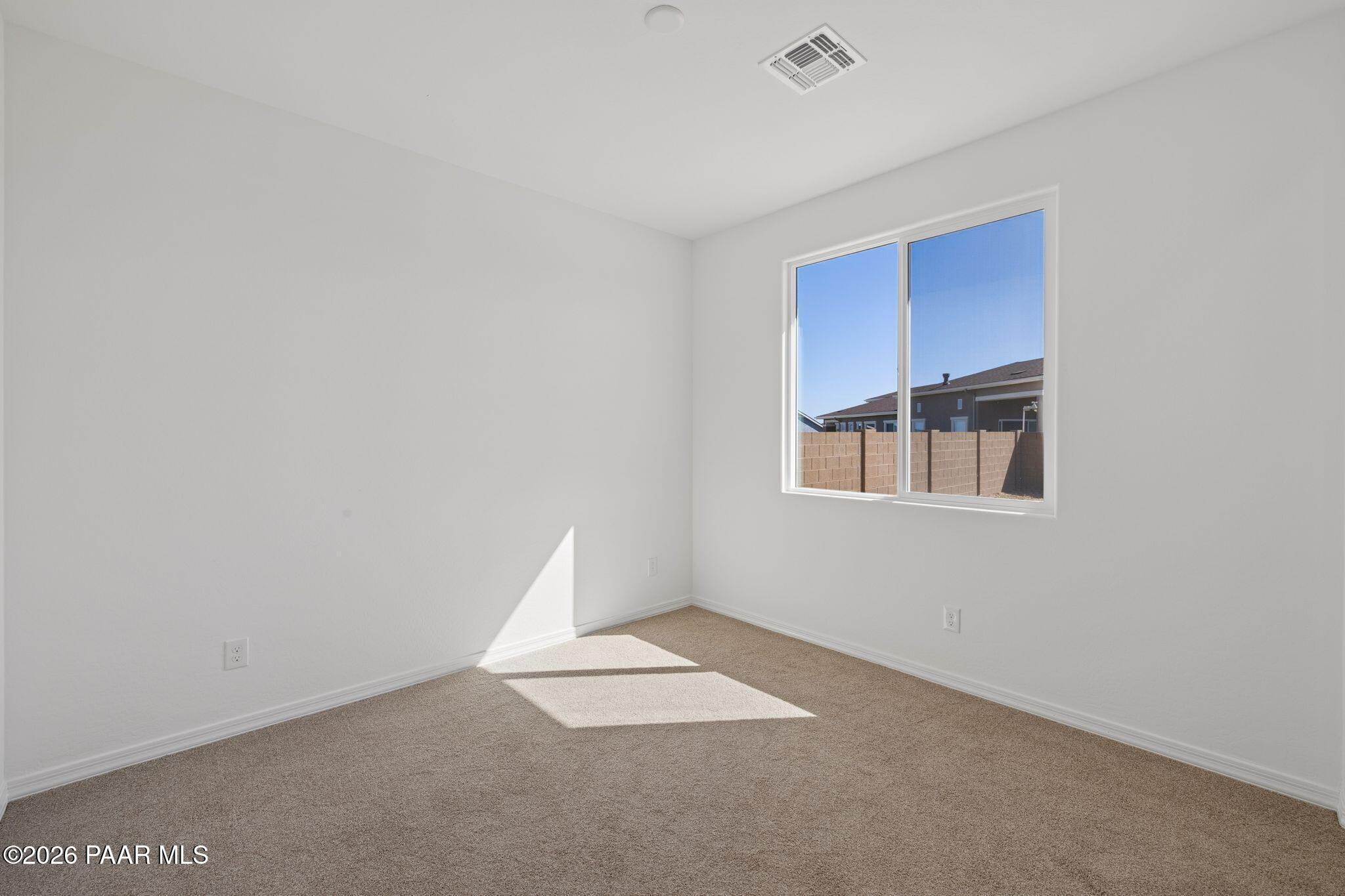 Bright empty bedroom with white walls, beige carpet, large window, and natural sunlight in Davidson Homes The Monarch A, Prescott, Arizona