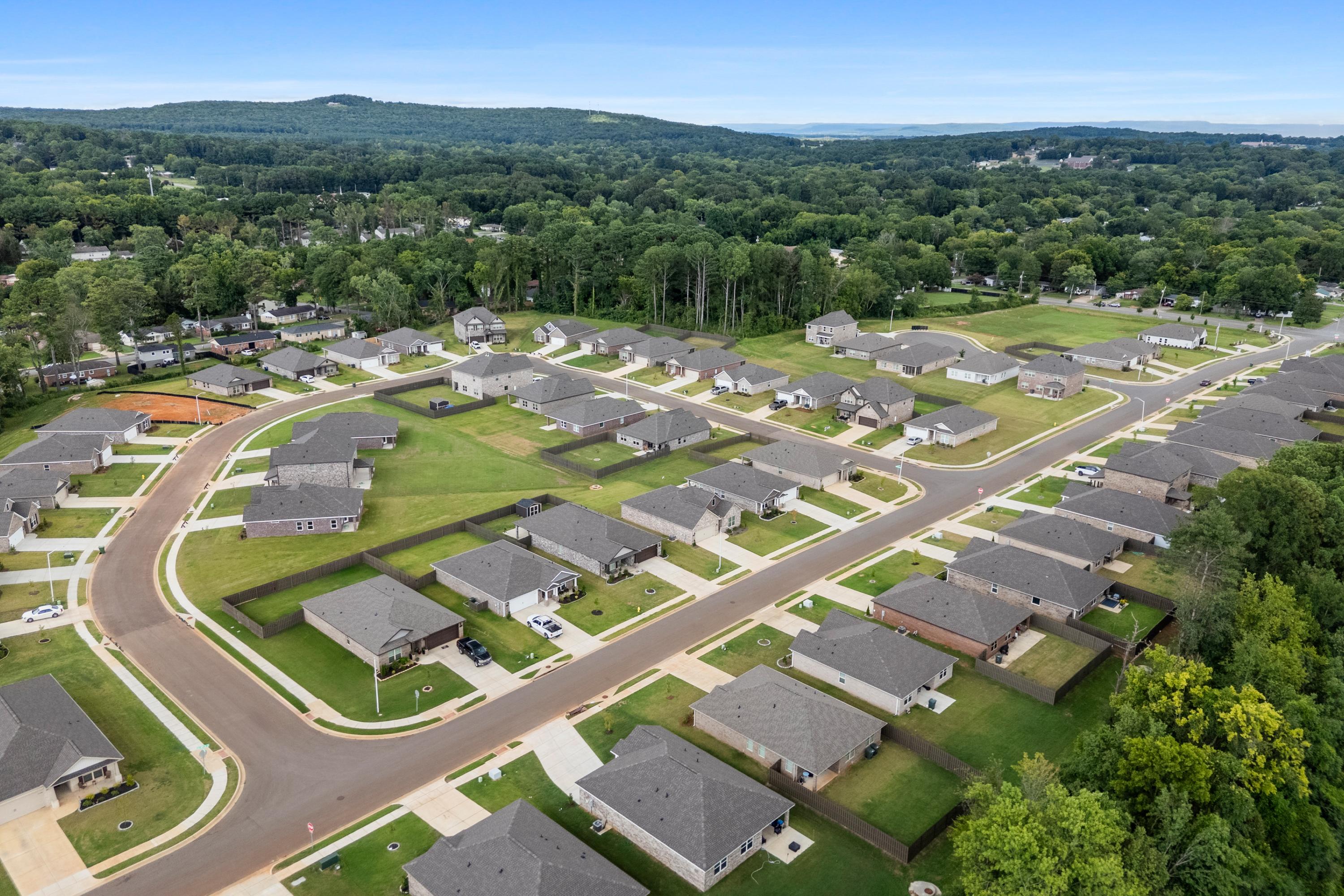 Aerial view of Blue Spring neighborhood in Huntsville AL with modern homes, curved streets, green lawns, and wooded hills