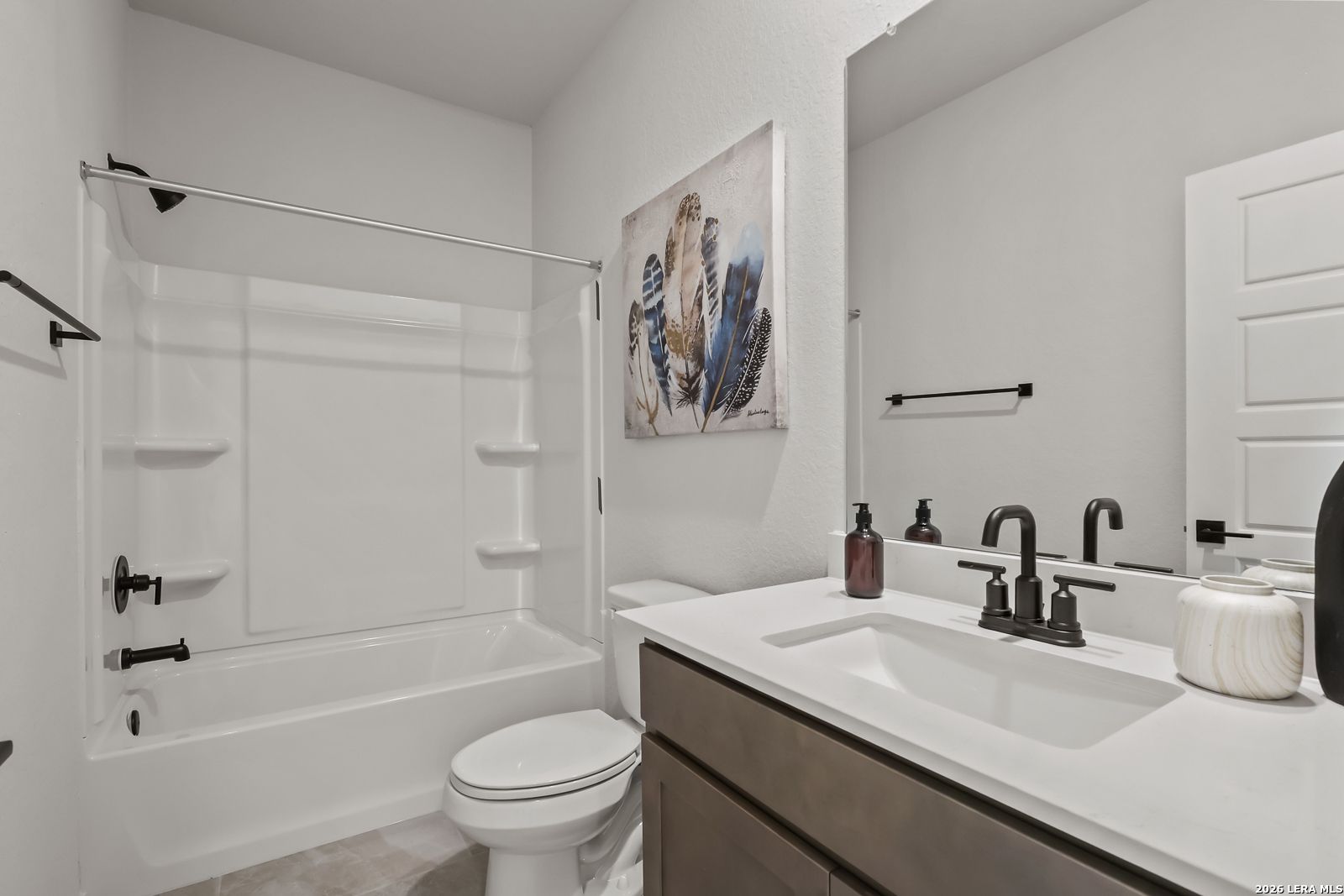 Modern bathroom with white tub-shower combo, black fixtures, abstract blue wall art in Davidson Homes The Daphne H, Seguin TX