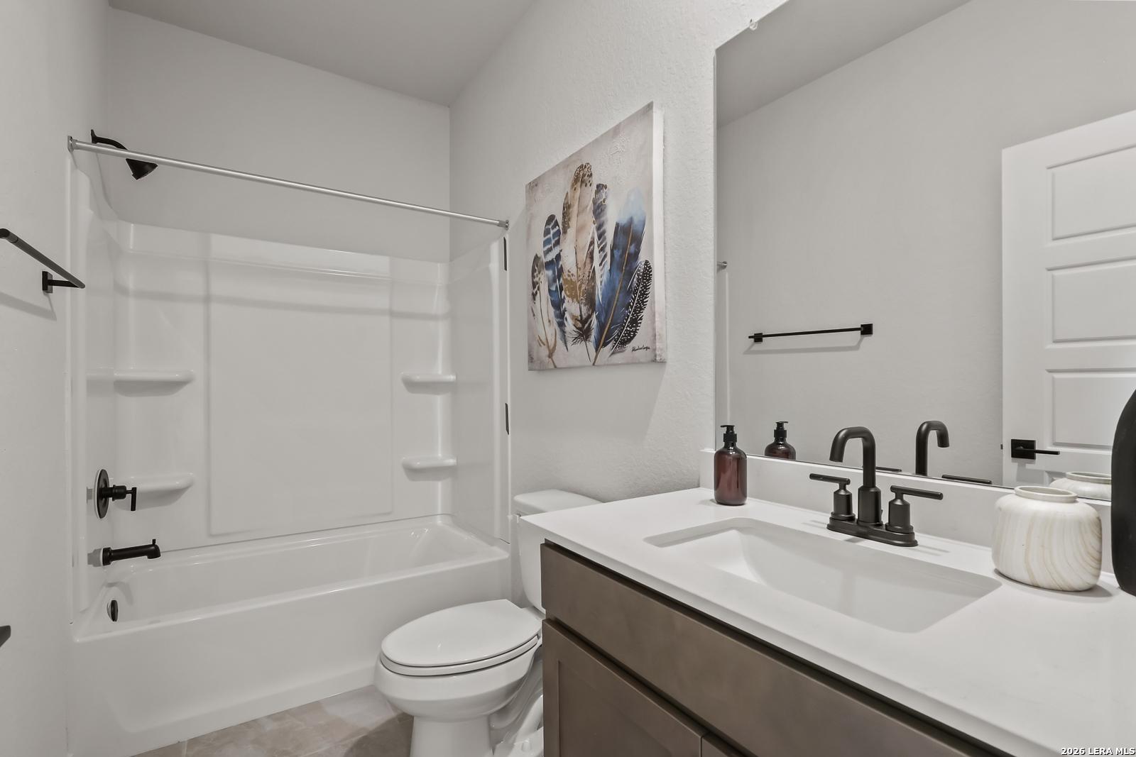 Modern bathroom with white tub-shower combo, black fixtures, abstract blue wall art in Davidson Homes The Daphne H, Seguin TX