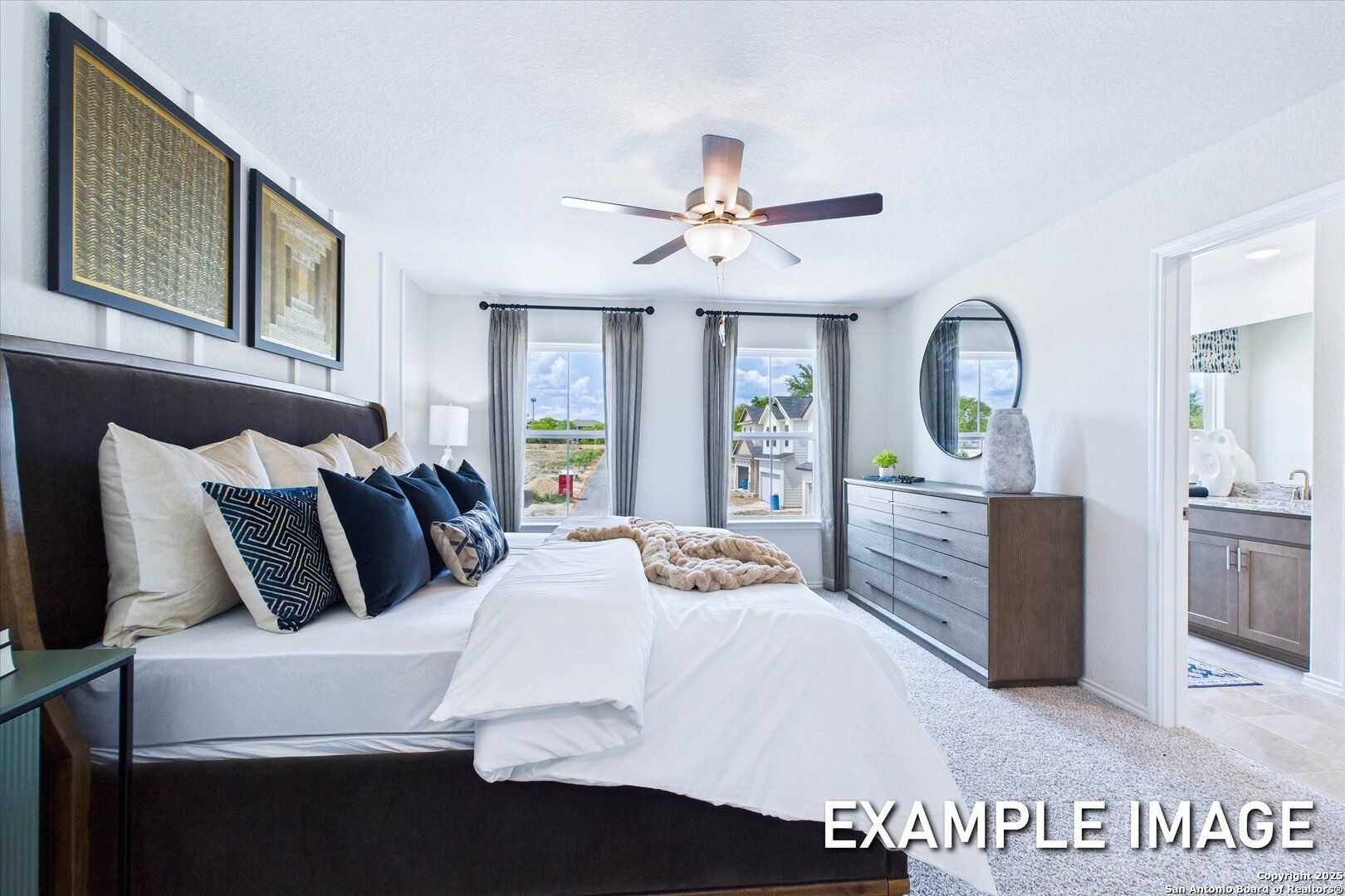 Elegant master bedroom with king bed, navy pillows, ceiling fan, and en-suite bath in Davidson Homes The Gillian B, San Antonio, Texas