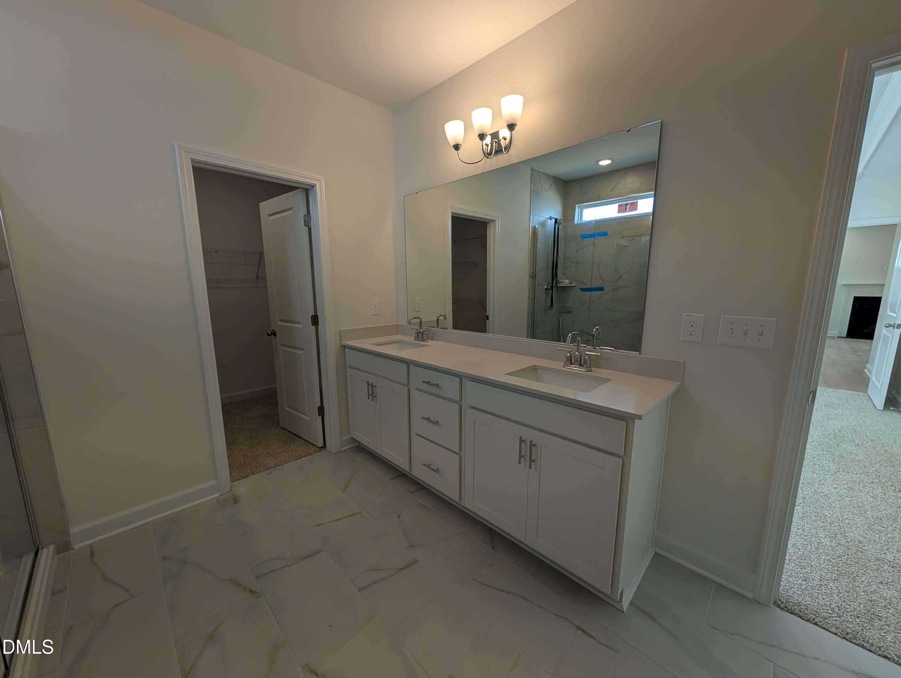 Double vanity bathroom with white cabinetry, large mirror, and marble tile in Davidson Homes Magnolia A, Wendell, NC