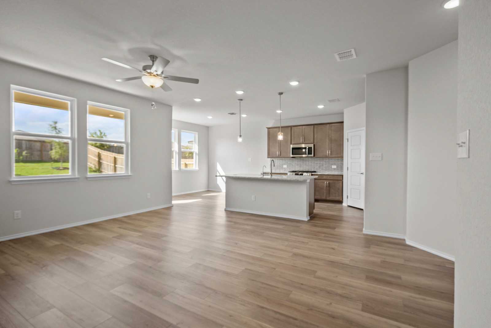 Open-concept kitchen with white island, stainless appliances, hardwood floors, and backyard views in The Redbud B, Josephine, Texas