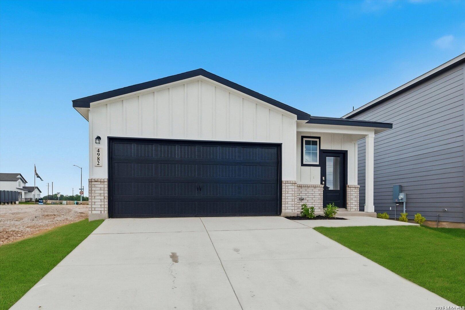 Modern 1-story The Frio B home by Davidson Homes with white shiplap siding, black 2-car garage, and front porch in Agave, San Antonio, Texas