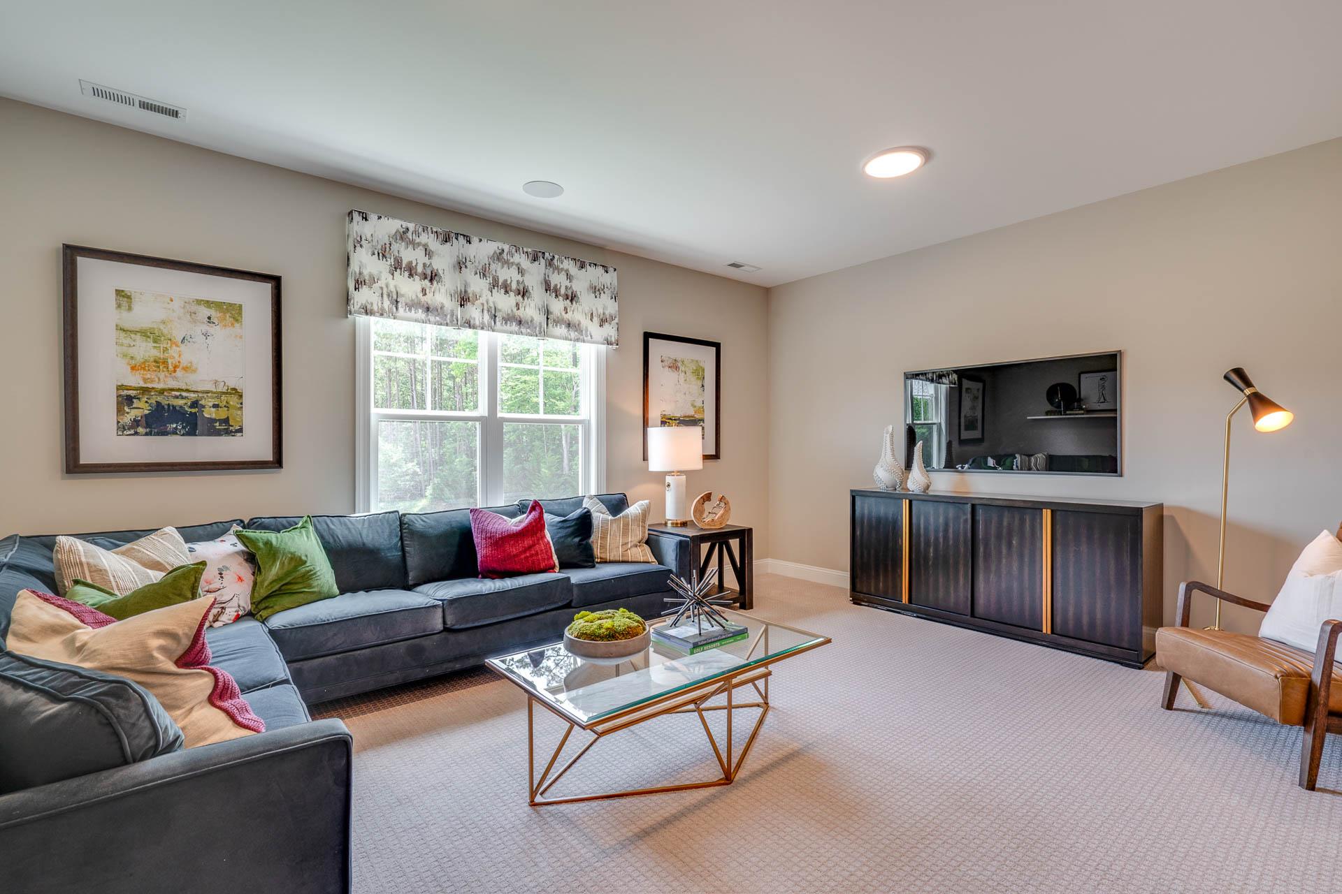 Cozy living room in Hasentree Wake Forest NC home with navy L-shaped sectional sofa, colorful pillows, glass coffee table, and wall TV