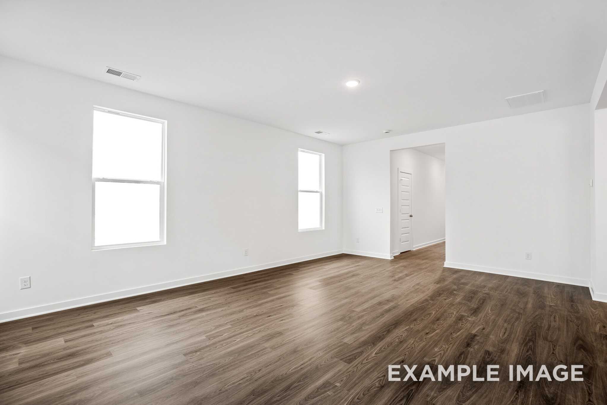 Spacious empty living room in The Grayson C with hardwood floors, large windows, white walls, and open doorway