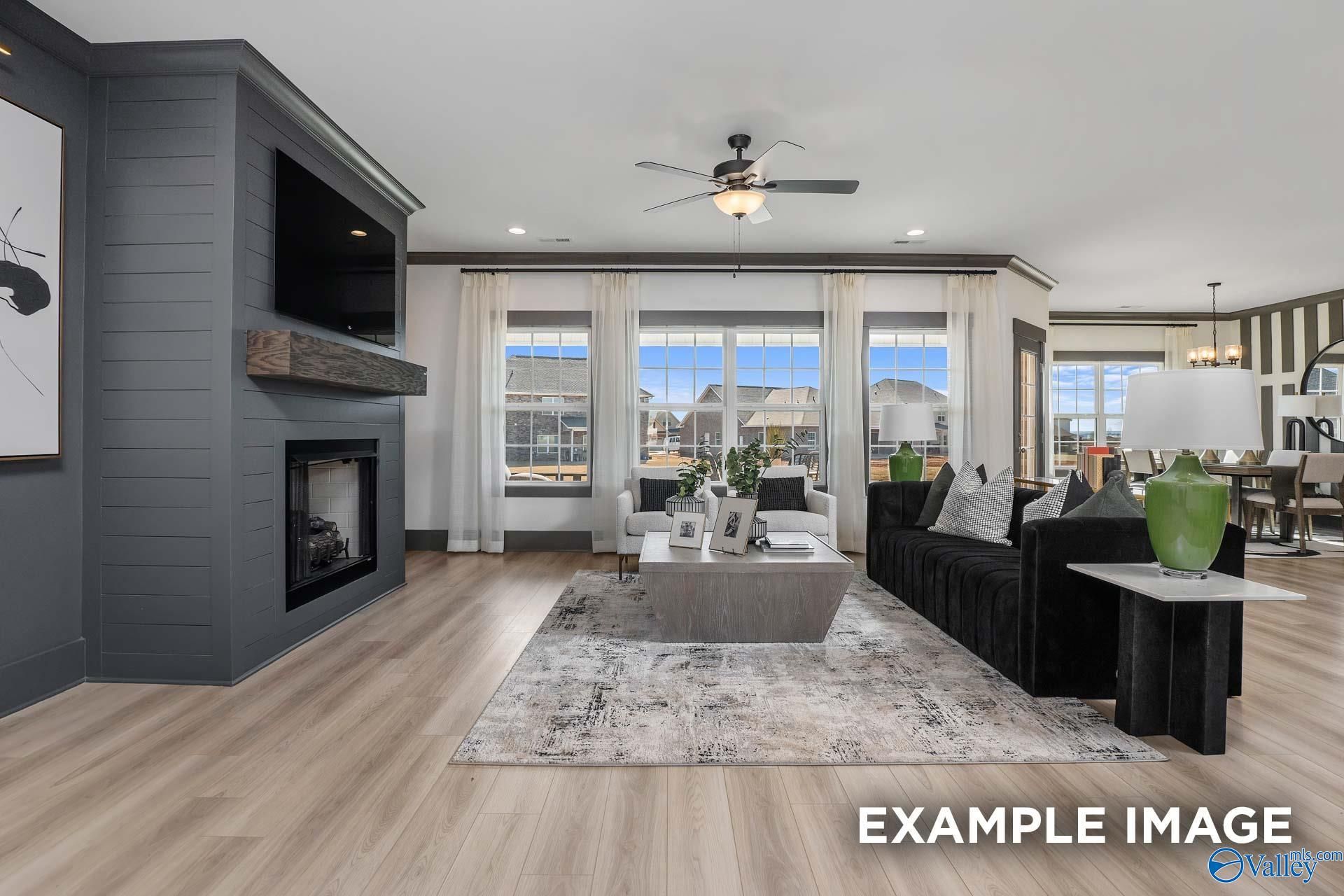 Cozy great room with gray shiplap fireplace, mounted TV, black leather sofa, and large windows in Davidson Homes The Rockford B, Madison AL
