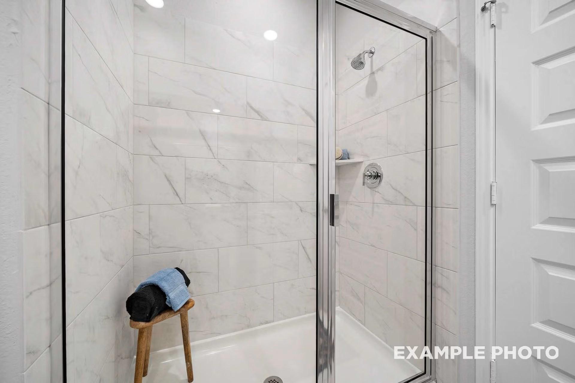 Modern walk-in shower with white marble-look tile and glass door in The San Marcos E floor plan, Heartland, Texas.
