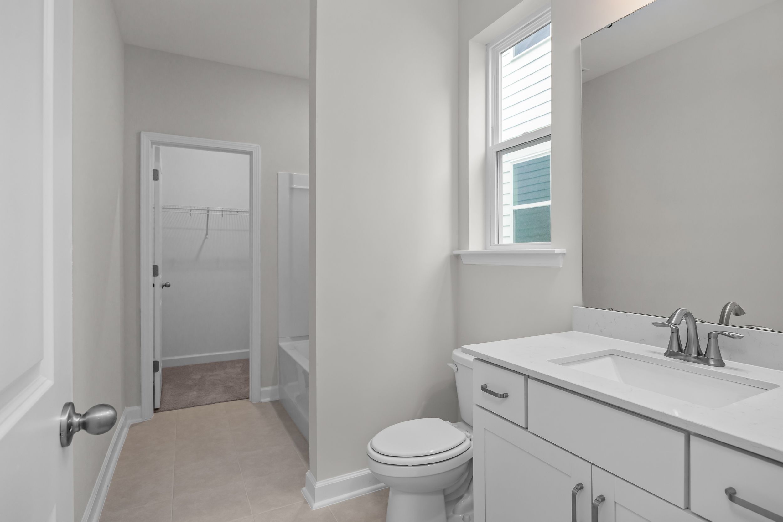 Spacious upper-floor bathroom in The Aspen B showcasing white vanity sink, toilet, walk-in closet, and window