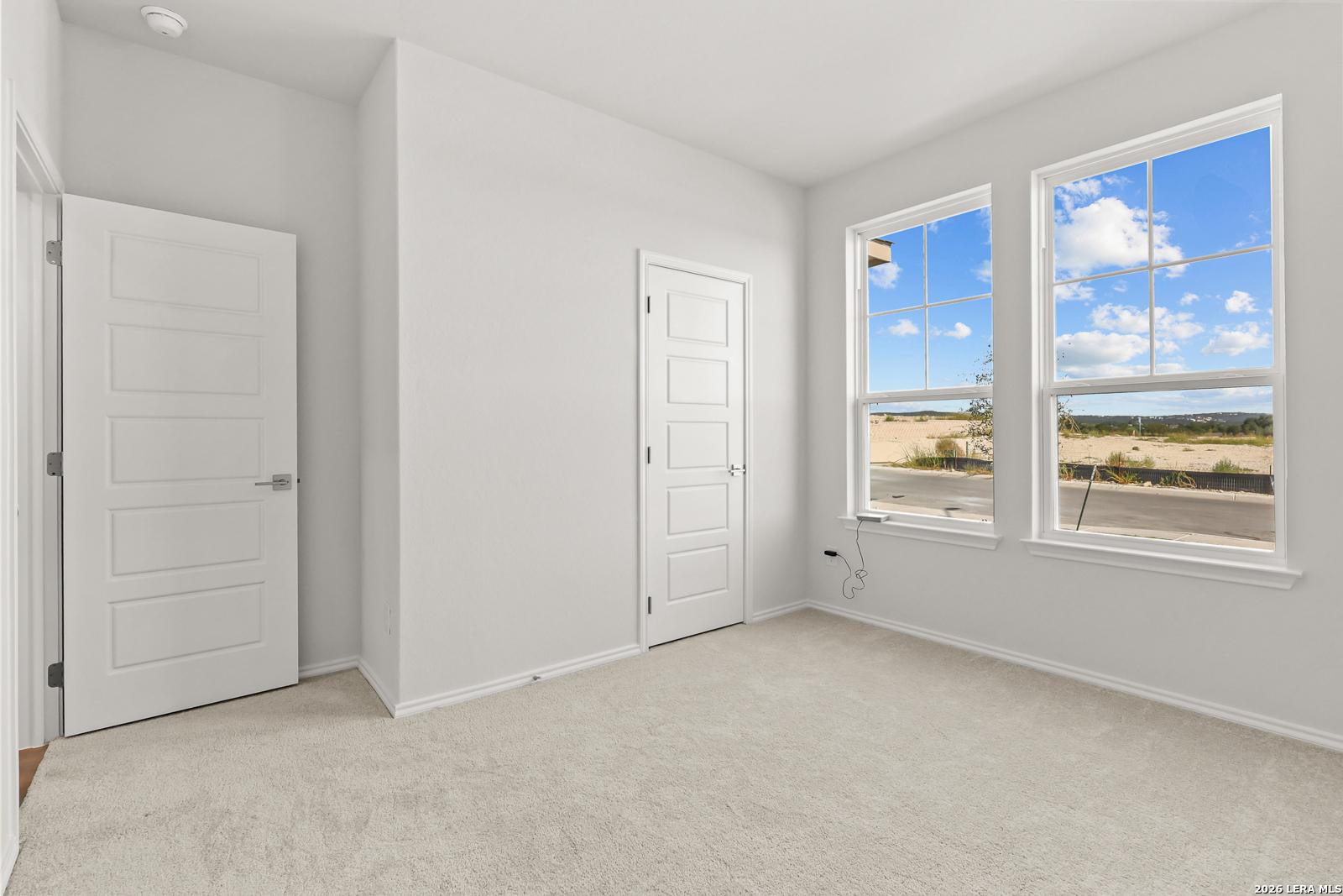 Bright carpeted bedroom with white doors and large windows at Davidson Homes' The Daphne I in Bricewood, San Antonio, Texas