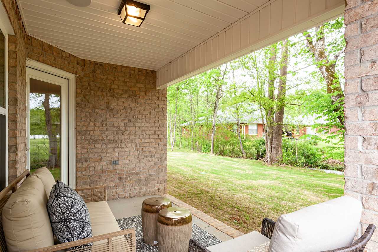 Spacious covered patio of The Franklin home with beige brick walls, outdoor sofa, chairs, and lush green backyard view