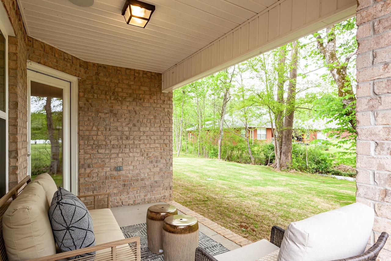 Spacious covered patio of The Franklin C home with brick walls, French doors, beige sofa, wicker chair, and lush green backyard in Meridianville