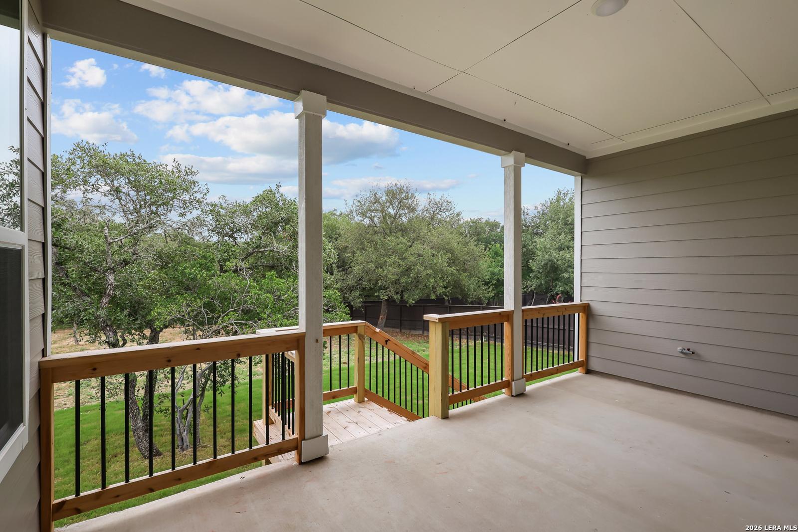 Covered porch with white columns, wooden railing, and steps to lush green backyard in Davidson Homes The Belmont H, Castroville, Texas