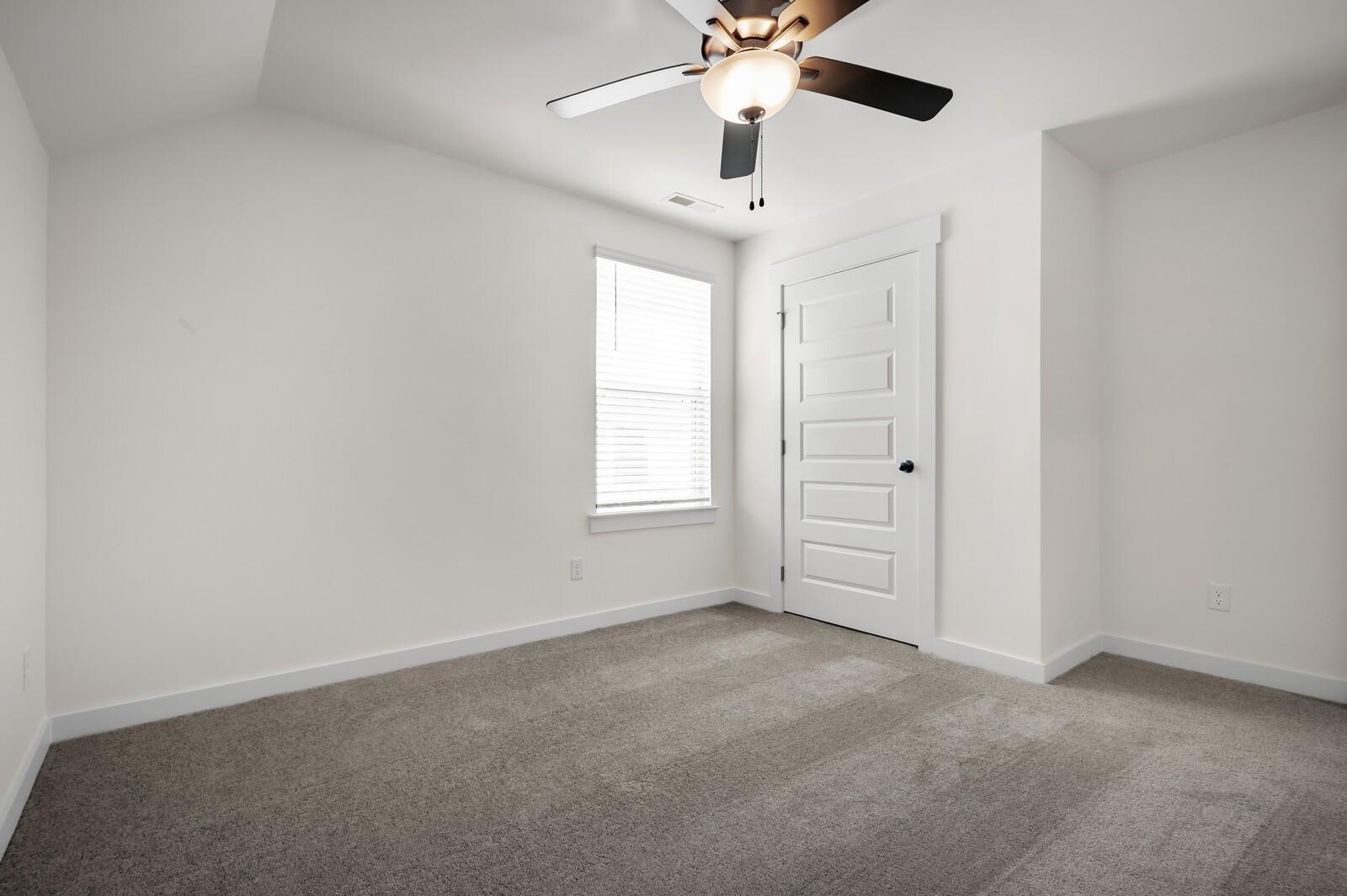Bright, carpeted bedroom with ceiling fan in The Ash A floor plan at Woods Crossing, Gallatin, Tennessee.