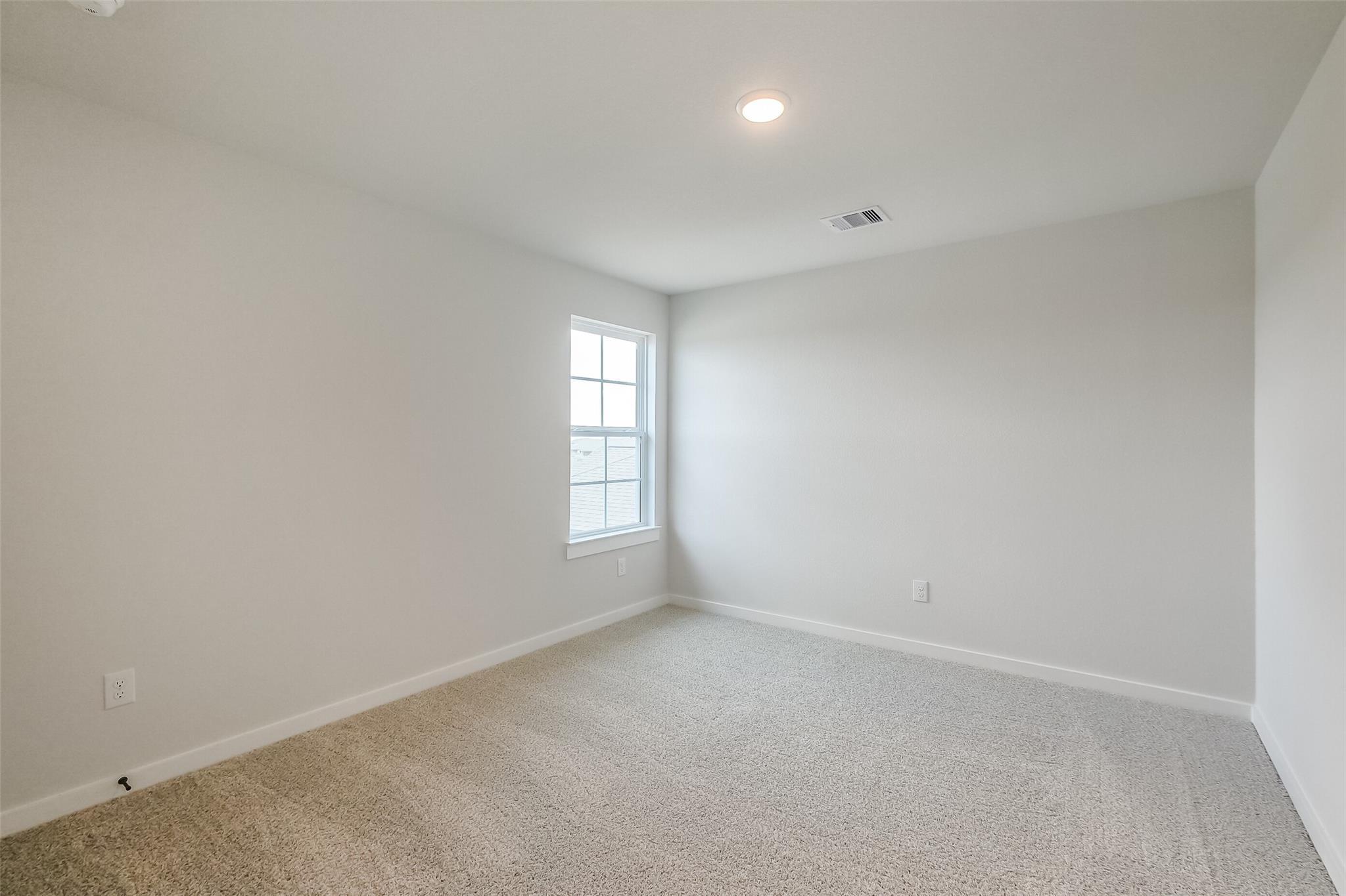 Bright secondary bedroom with neutral walls, beige carpet, and double window in Davidson Homes The Tierra B, Beasley, Texas