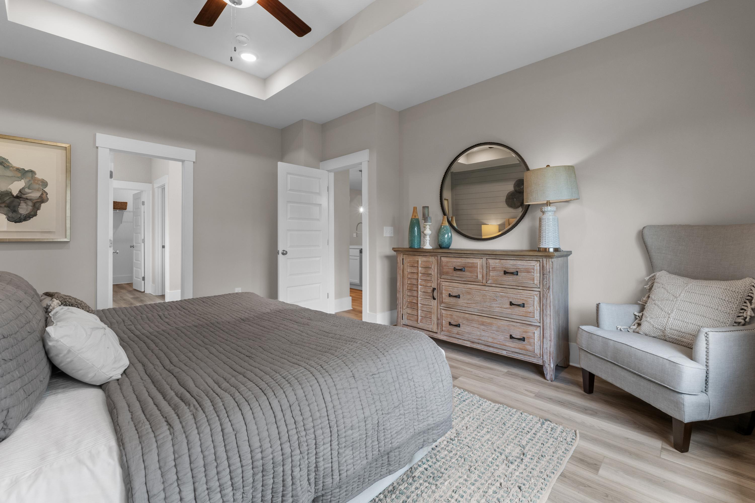 Spacious primary bedroom in The Highlands, Arab AL with gray king bed, wooden dresser, round mirror, and accent chair