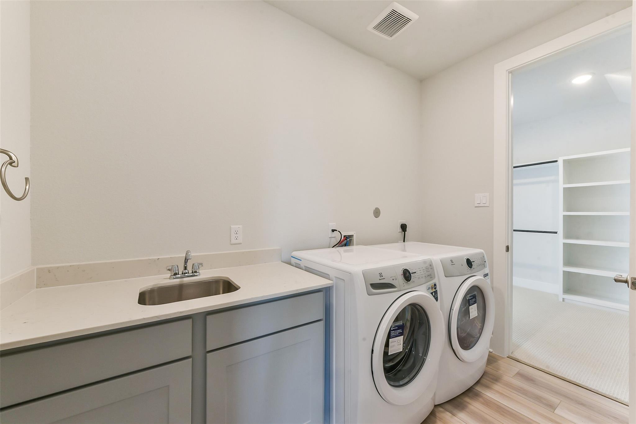 Modern laundry room with white front-load washer dryer, utility sink, gray cabinets, and open shelving in Davidson Homes The Edward A, Lago Mar, Texas City