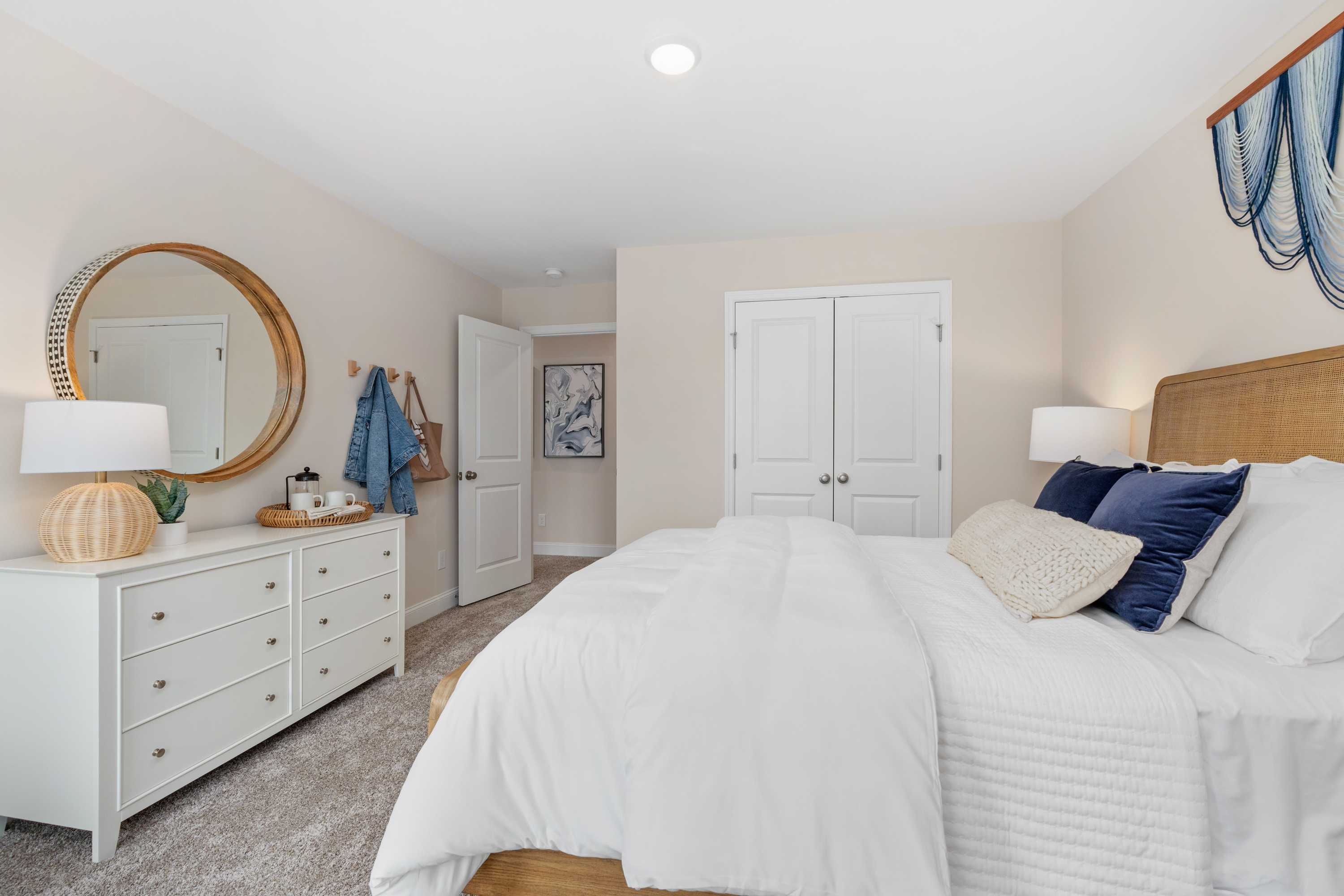 Spacious primary bedroom at Pavilion in Huntsville AL with king bed white duvet blue pillows gold mirror white dresser and walk-in closet