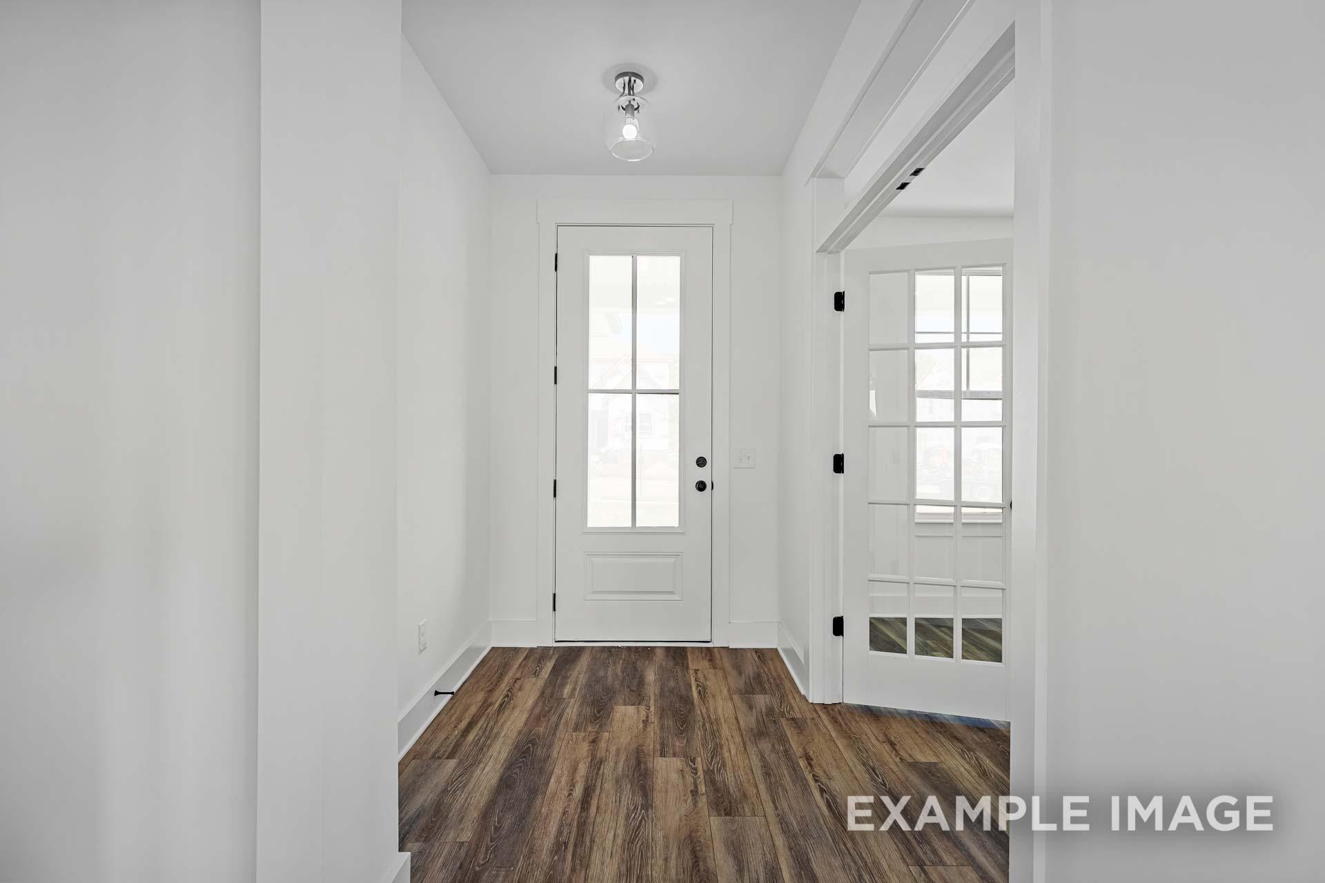 Spacious entryway in The Ash C home featuring white walls, warm hardwood floors, and glass-paneled white doors