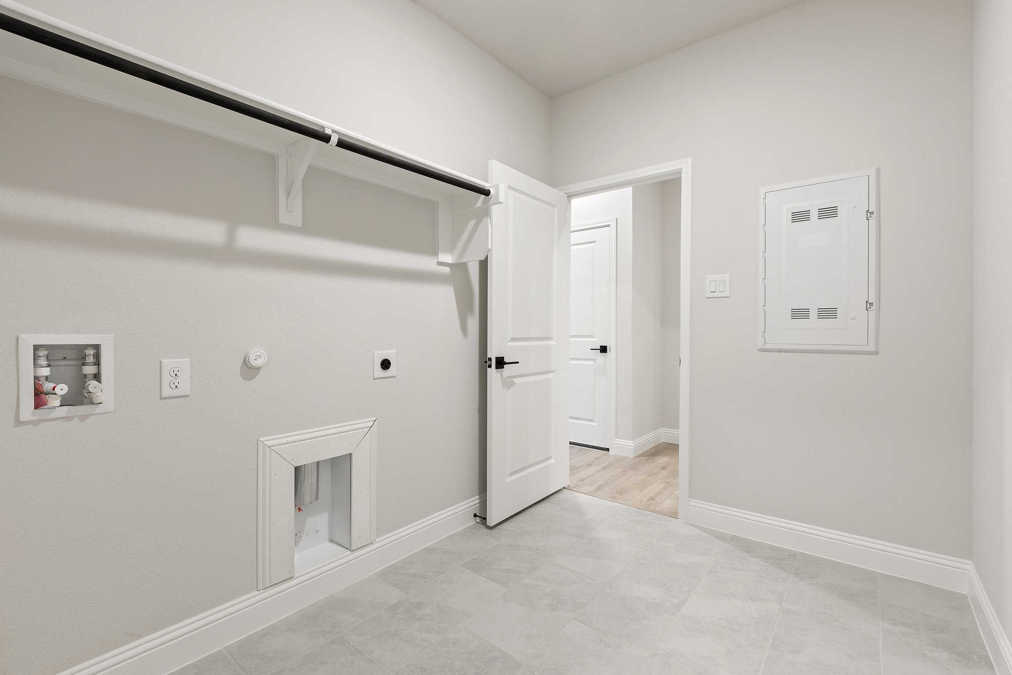 Spacious laundry room in The Harrison C featuring open white shelving, washer-dryer hookups, and utility door