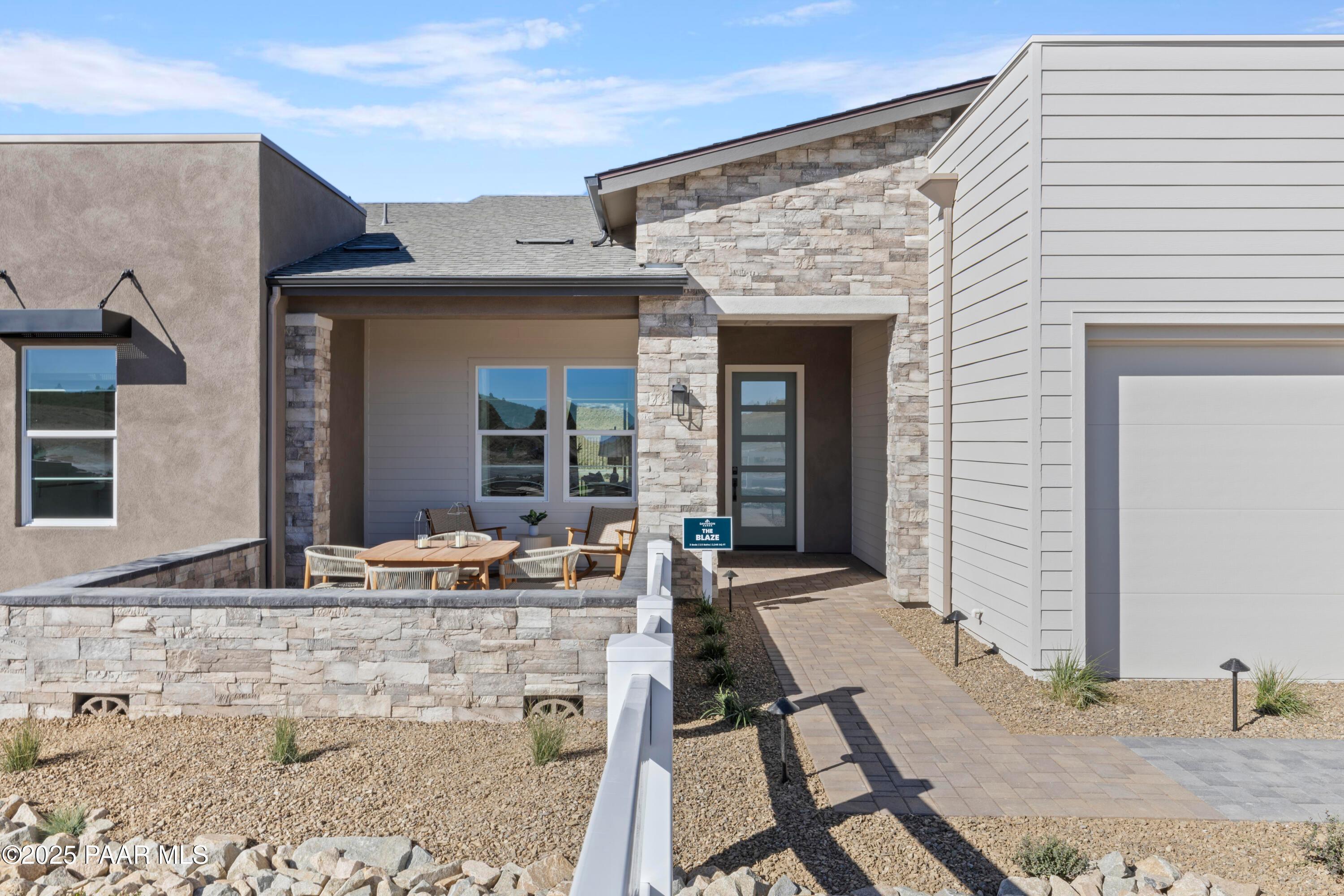 Modern stone and stucco single-story home with covered front porch, outdoor seating, and 3-car garage in Hidden Hills, Prescott, Arizona