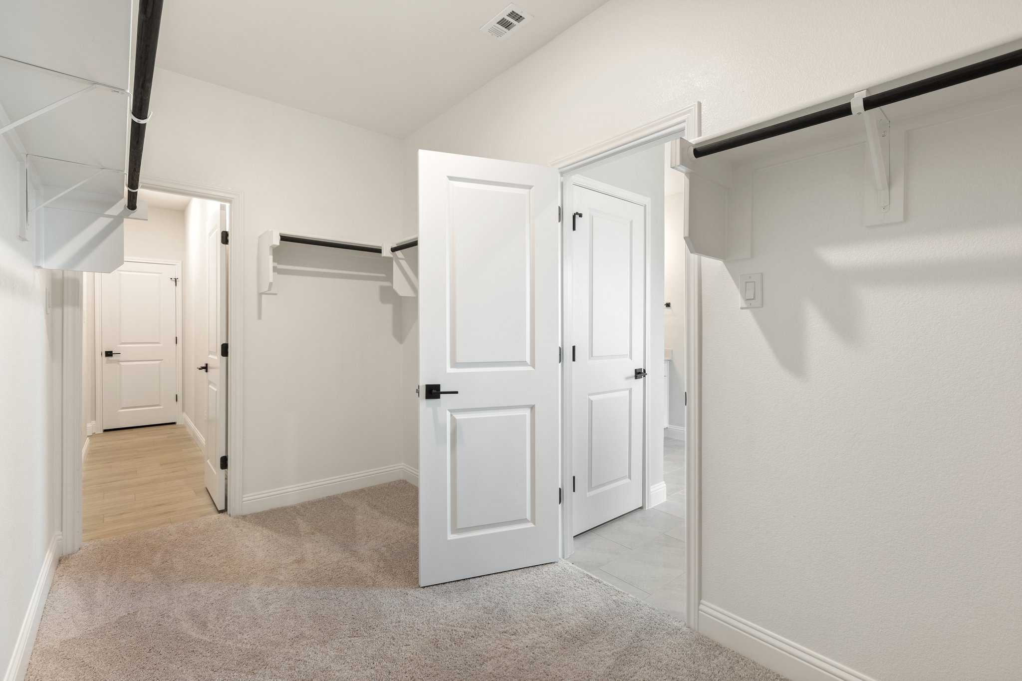 Spacious walk-in closet in The Harrison master suite with white walls, custom shelving, hanging rods, and open double doors