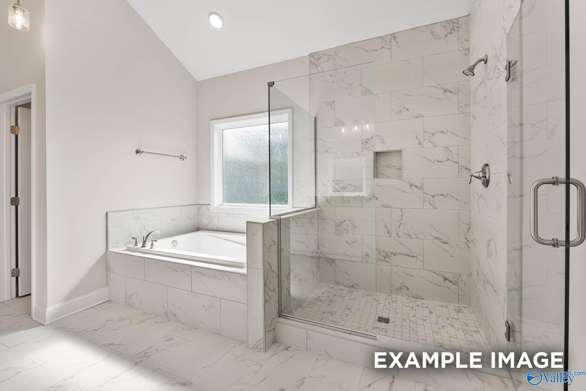 Elegant master bathroom with white marble tiles, frameless glass shower, and soaking tub in Davidson Homes The Finleigh, Huntsville, Alabama
