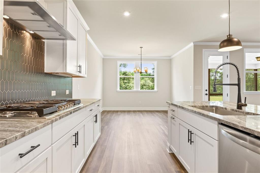 Open-concept kitchen with white shaker cabinets, hexagonal backsplash, quartz island, and stainless appliances in Harrison G home, Hoschton GA