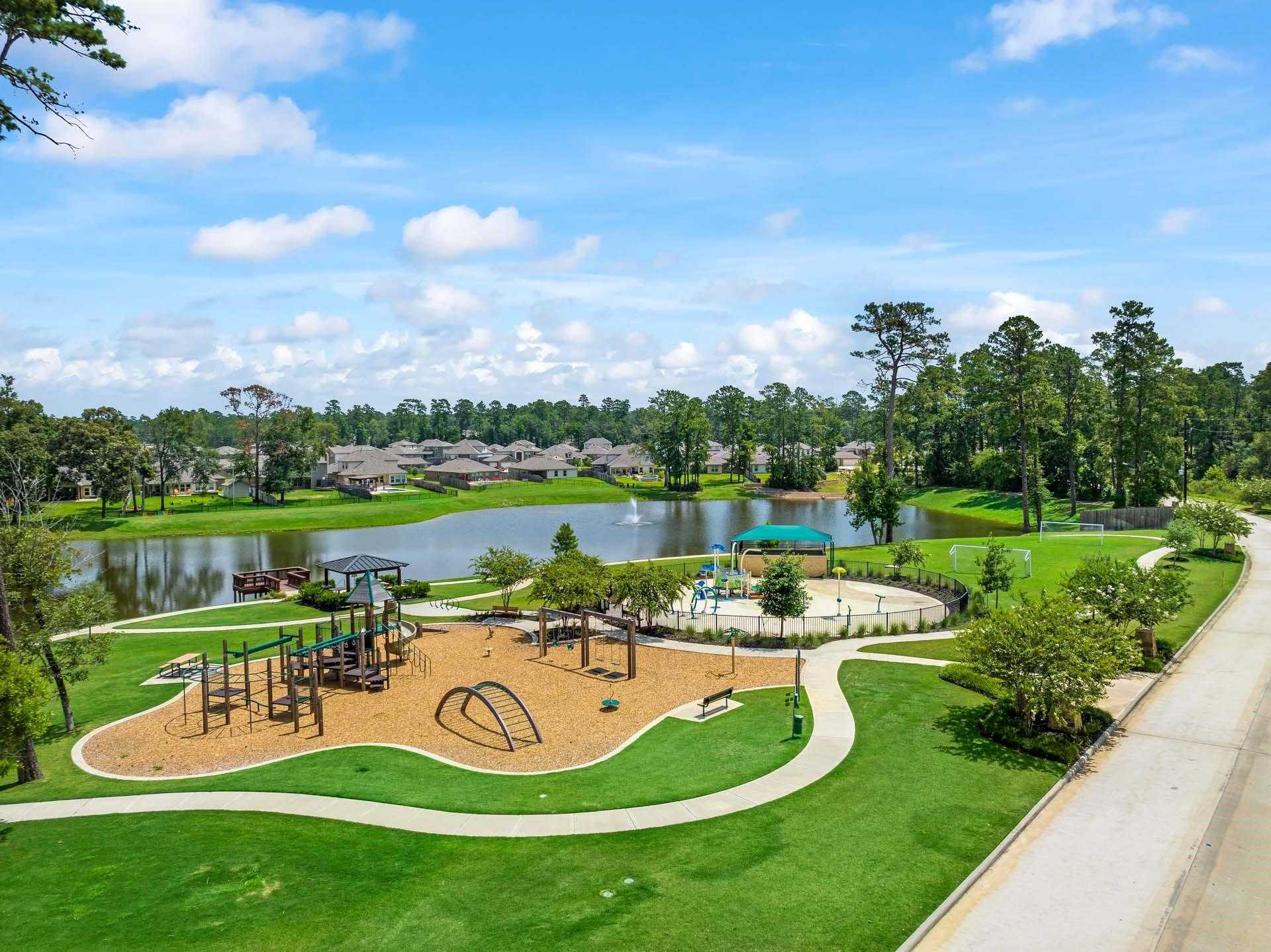 Playground with slides, swings, and climbing structures beside lake gazebo in Lakes at Black Oak, Magnolia, Texas