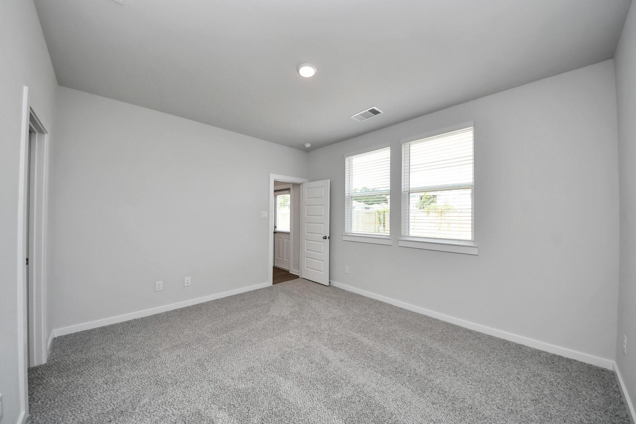 Bright empty bedroom with gray carpet, white walls, and two windows in Davidson Homes The Frio F plan at Robins Landing, Houston