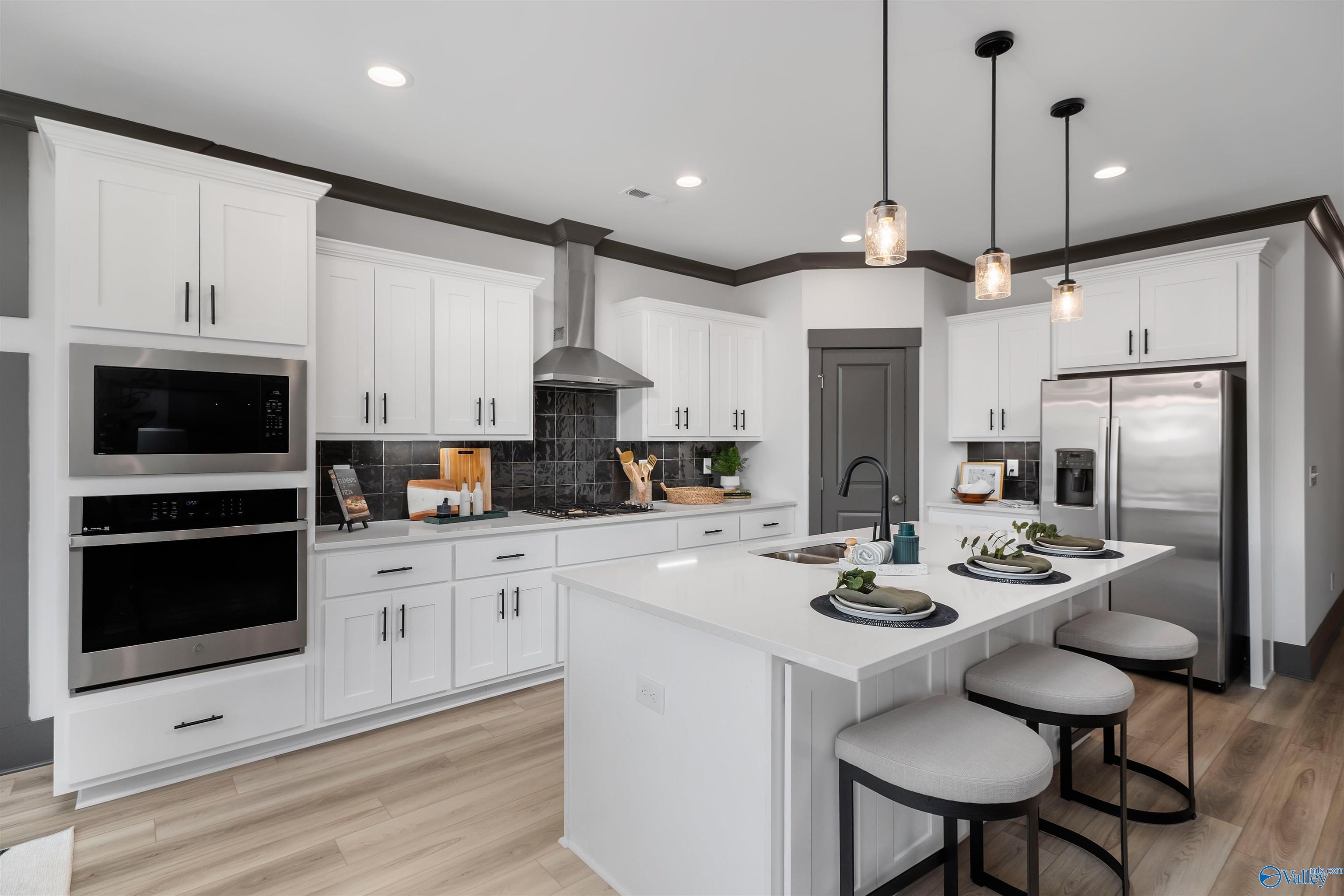 Modern white kitchen with stainless steel appliances, large island, and pendant lights in Davidson Homes The Rockford B, Madison, Alabama