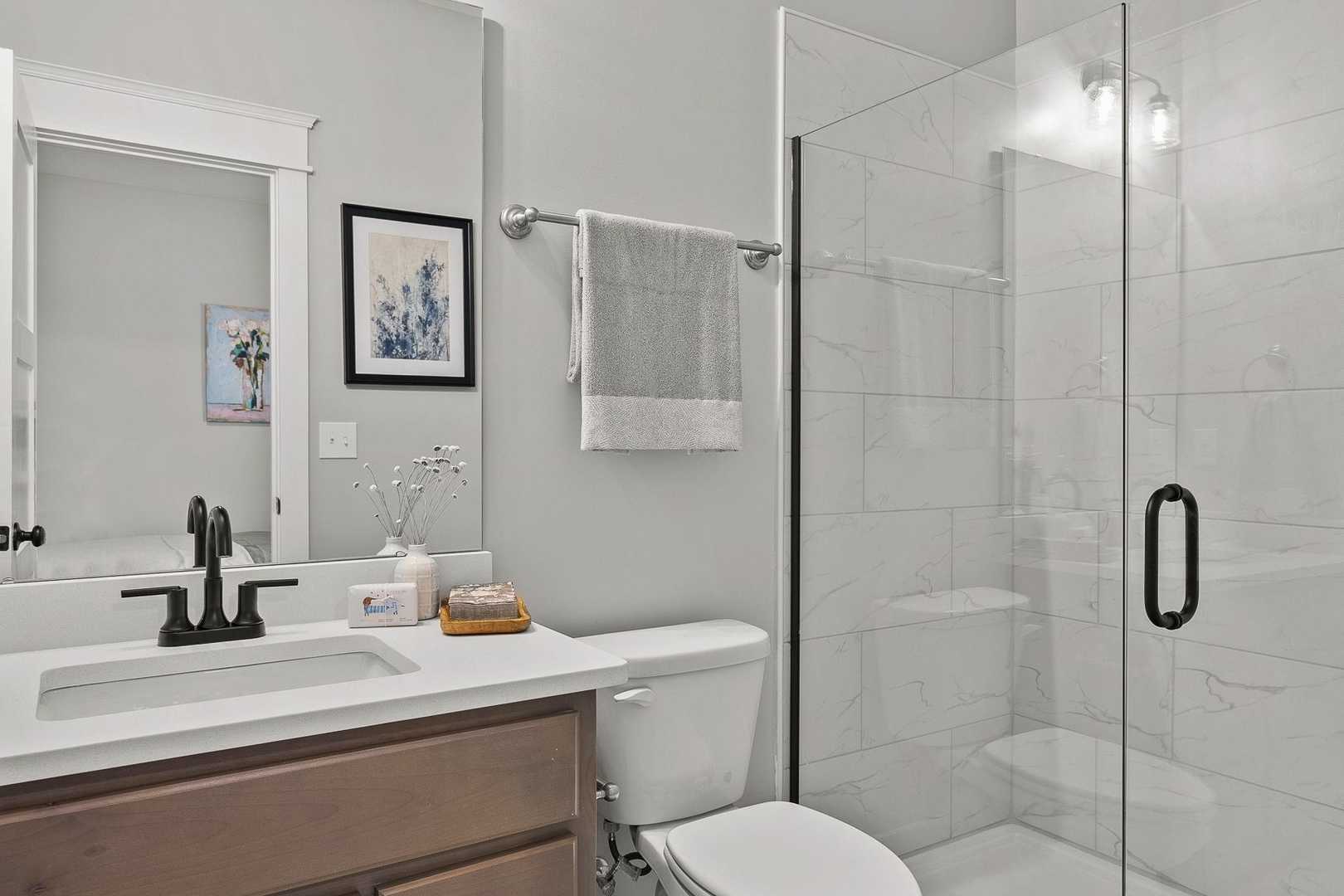 Modern master bathroom in The Oxford: frameless glass shower, white subway tile, wood vanity, and single sink