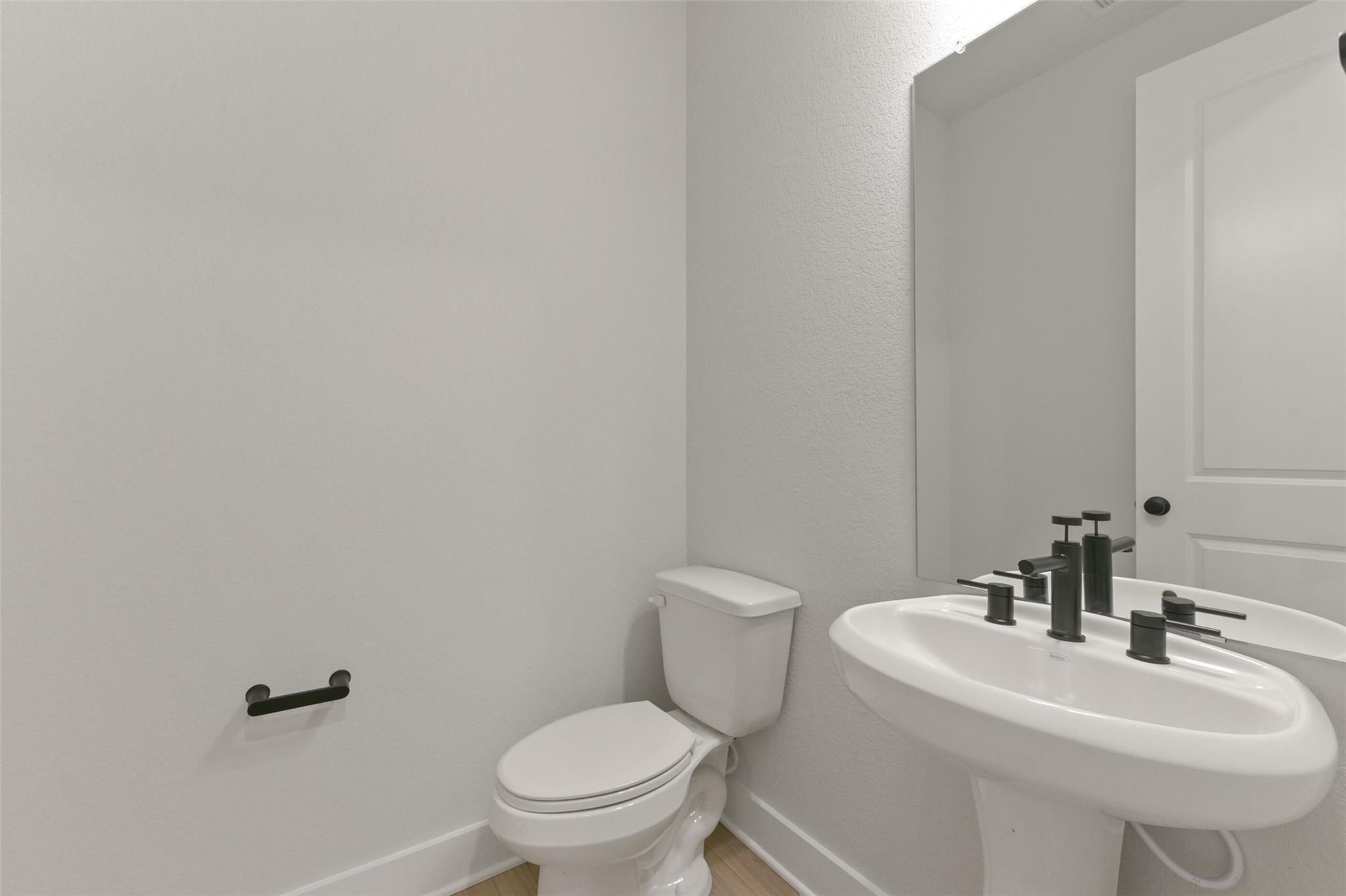 Modern half bath with white pedestal sink, black faucets, toilet, and grab bars in Davidson Homes The Edward C, Lago Mar, Texas City
