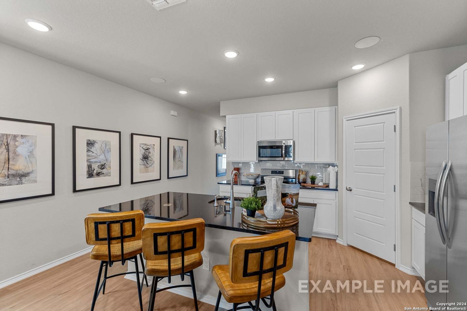 Modern kitchen with white cabinets, stainless appliances, dark island, and orange stools in Davidson Homes The Sabine B, San Antonio, Texas