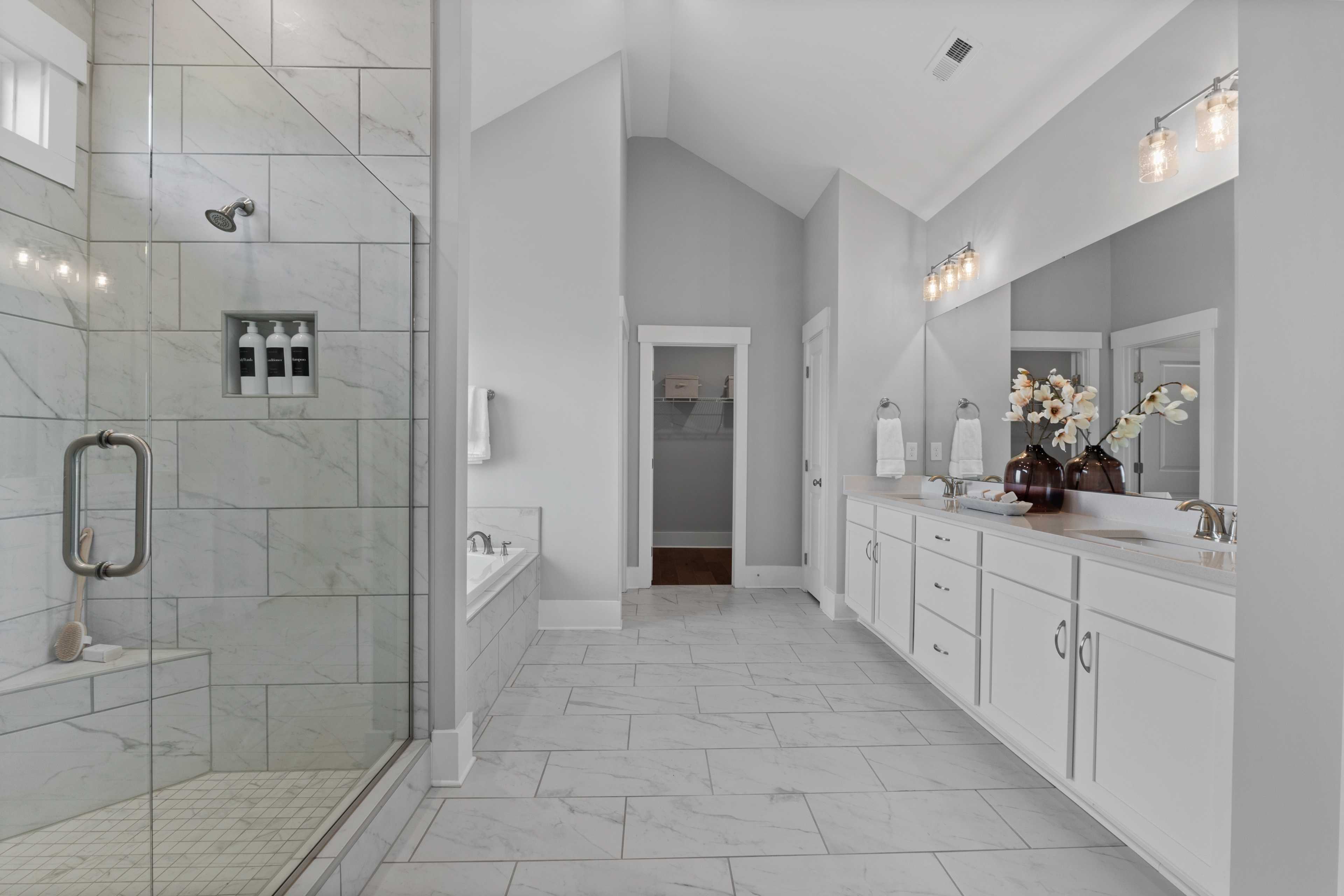 Spacious master bathroom in Creekside Harvest Alabama with glass shower, freestanding tub, double vanity, and tiled floors