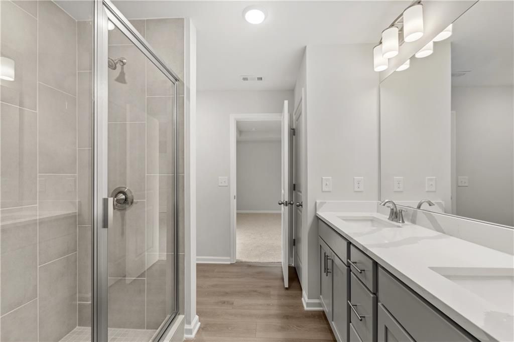 Modern primary bathroom with double vanity and walk-in glass shower in The Burton A plan at The Bluffs, Canton, Georgia.