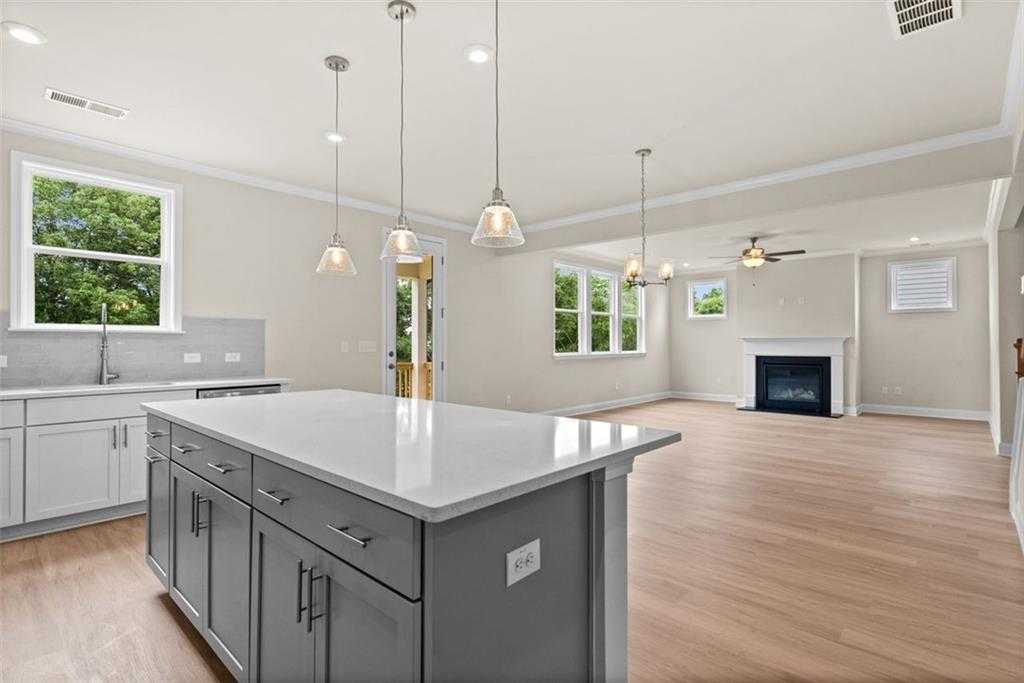 Modern open-concept kitchen with white quartz island, gas fireplace, and large windows in The Hickory B home at Wehunt Meadows, Hoschton