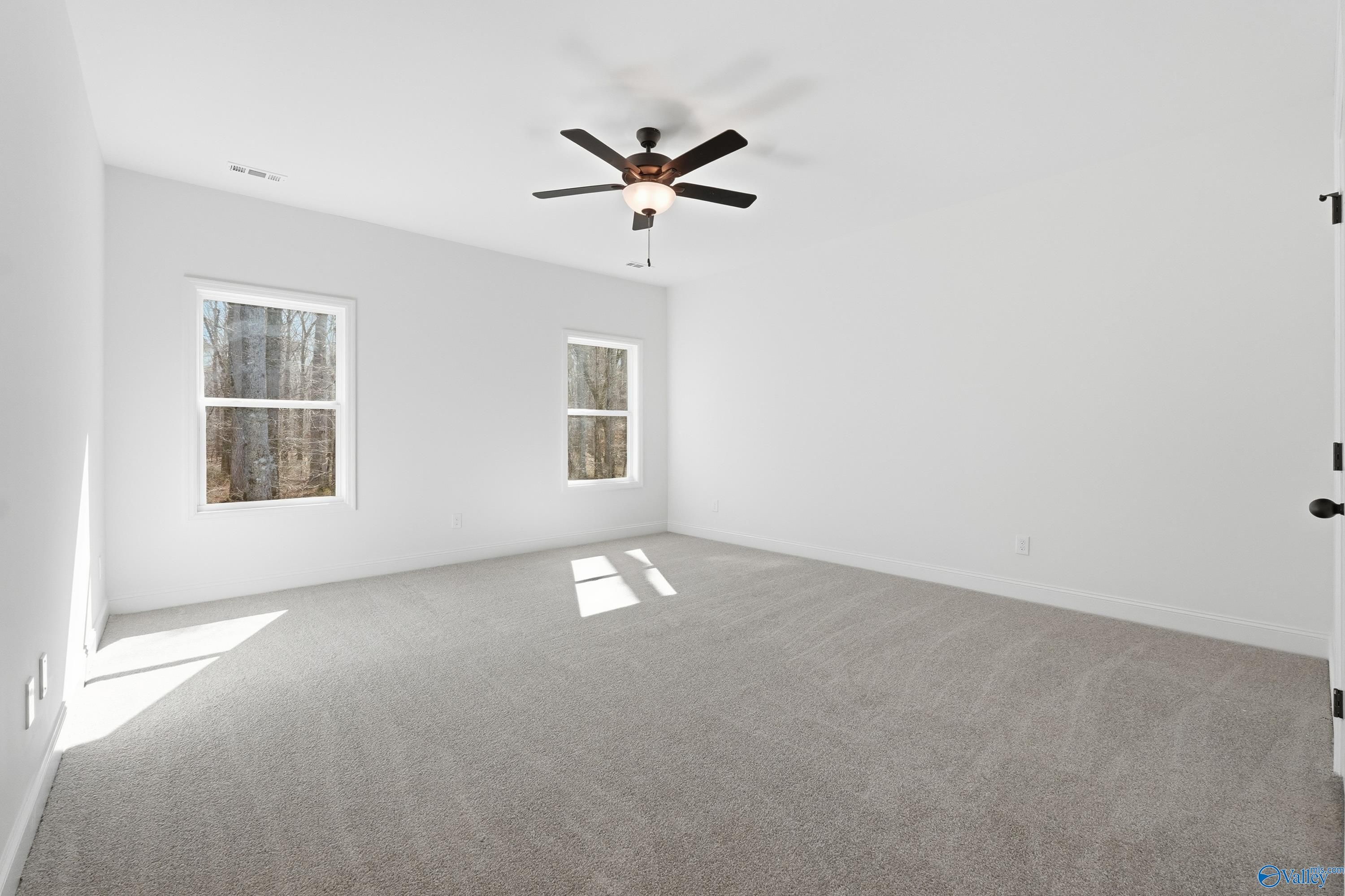 Bright bedroom with white walls, large windows showing wooded view, ceiling fan, and carpet in Davidson Homes The Rockford D, Hazel Green, Alabama