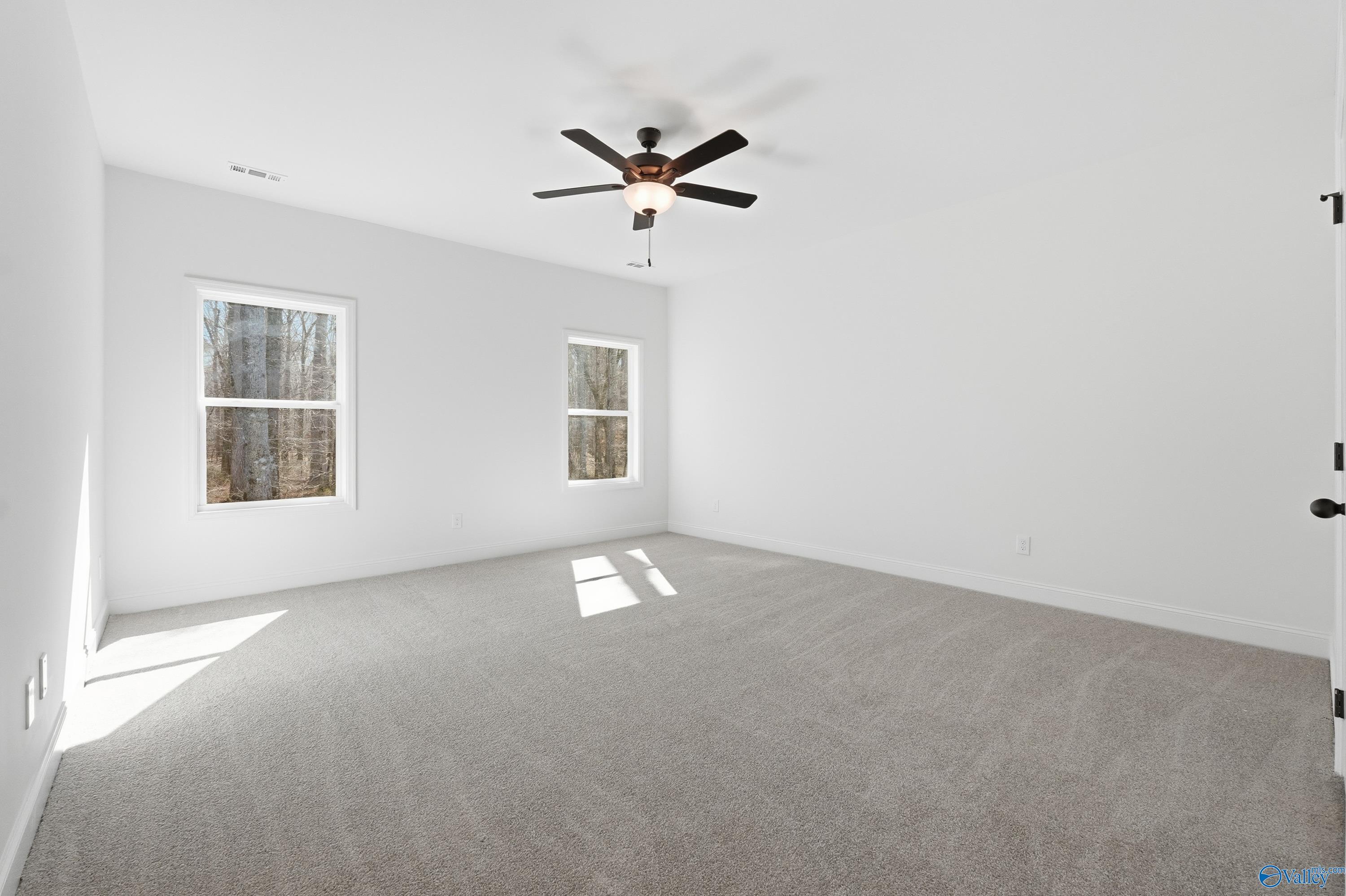 Bright bedroom with white walls, large windows showing wooded view, ceiling fan, and carpet in Davidson Homes The Rockford D, Hazel Green, Alabama