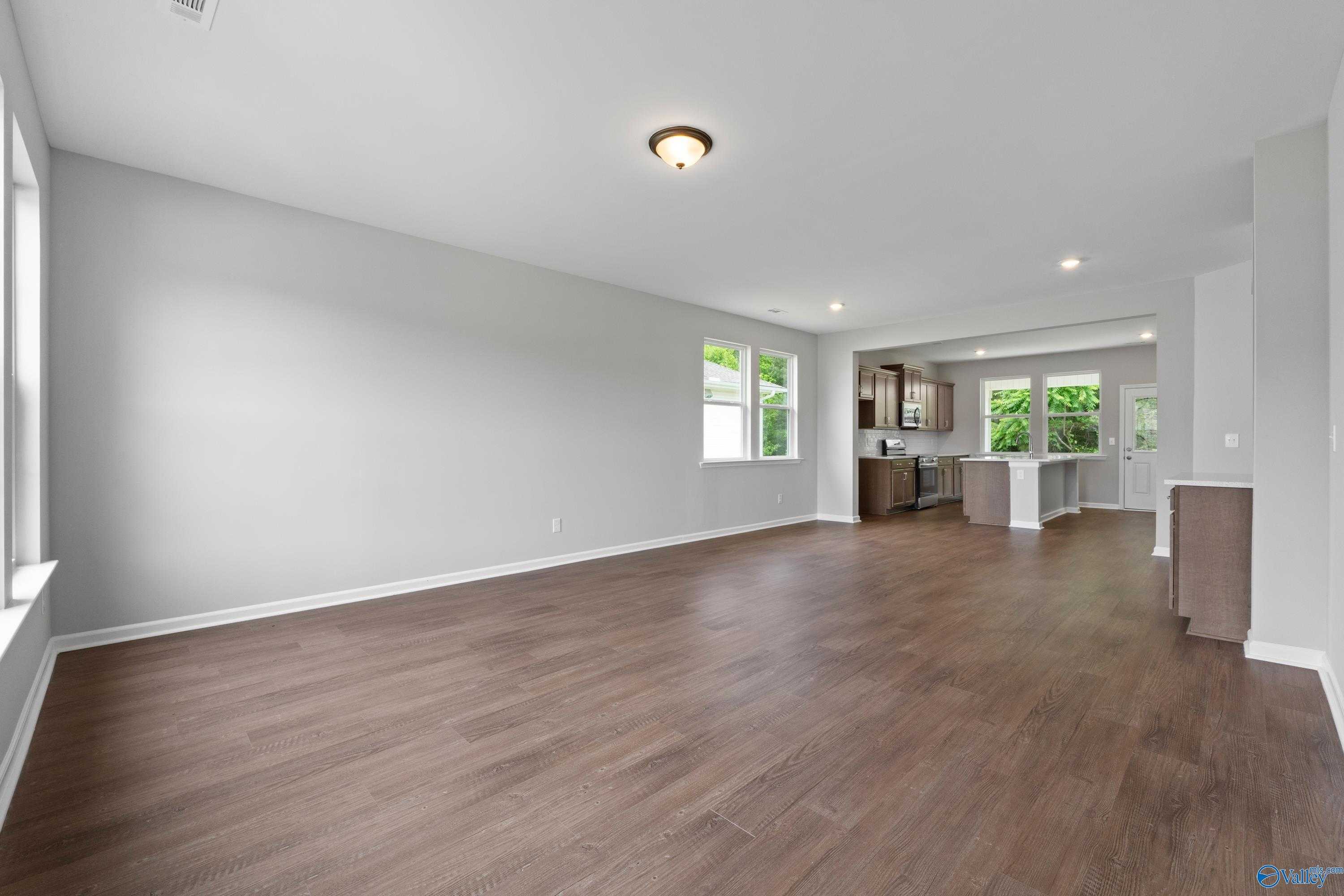 Open-concept great room and kitchen with hardwood floors, white cabinets, and large windows in Davidson Homes The Stella, Hazel Green, AL