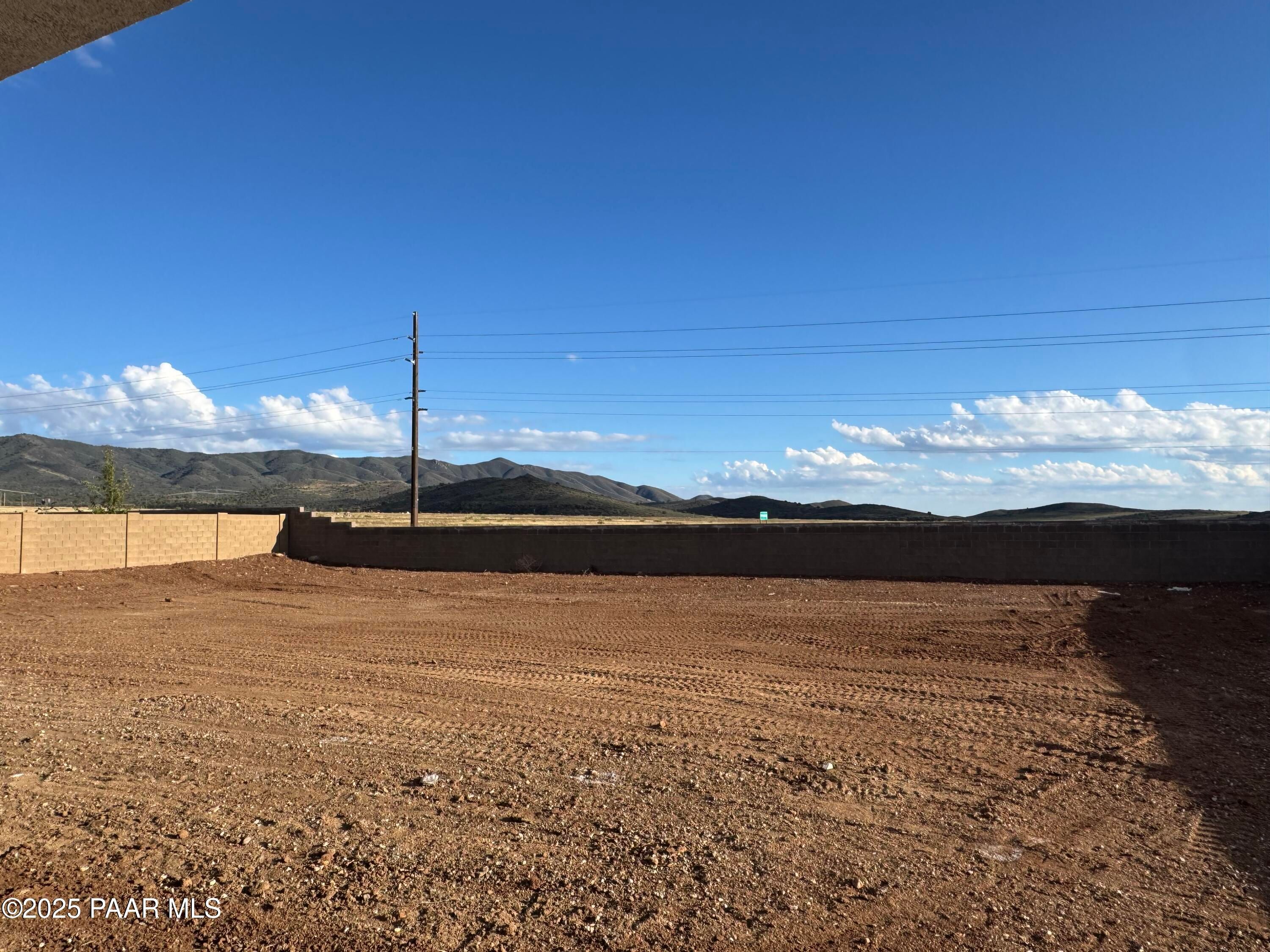 Graded dirt backyard lot with tan block fence, distant mountains, and utility pole under clear skies in Morningstar, Prescott Valley