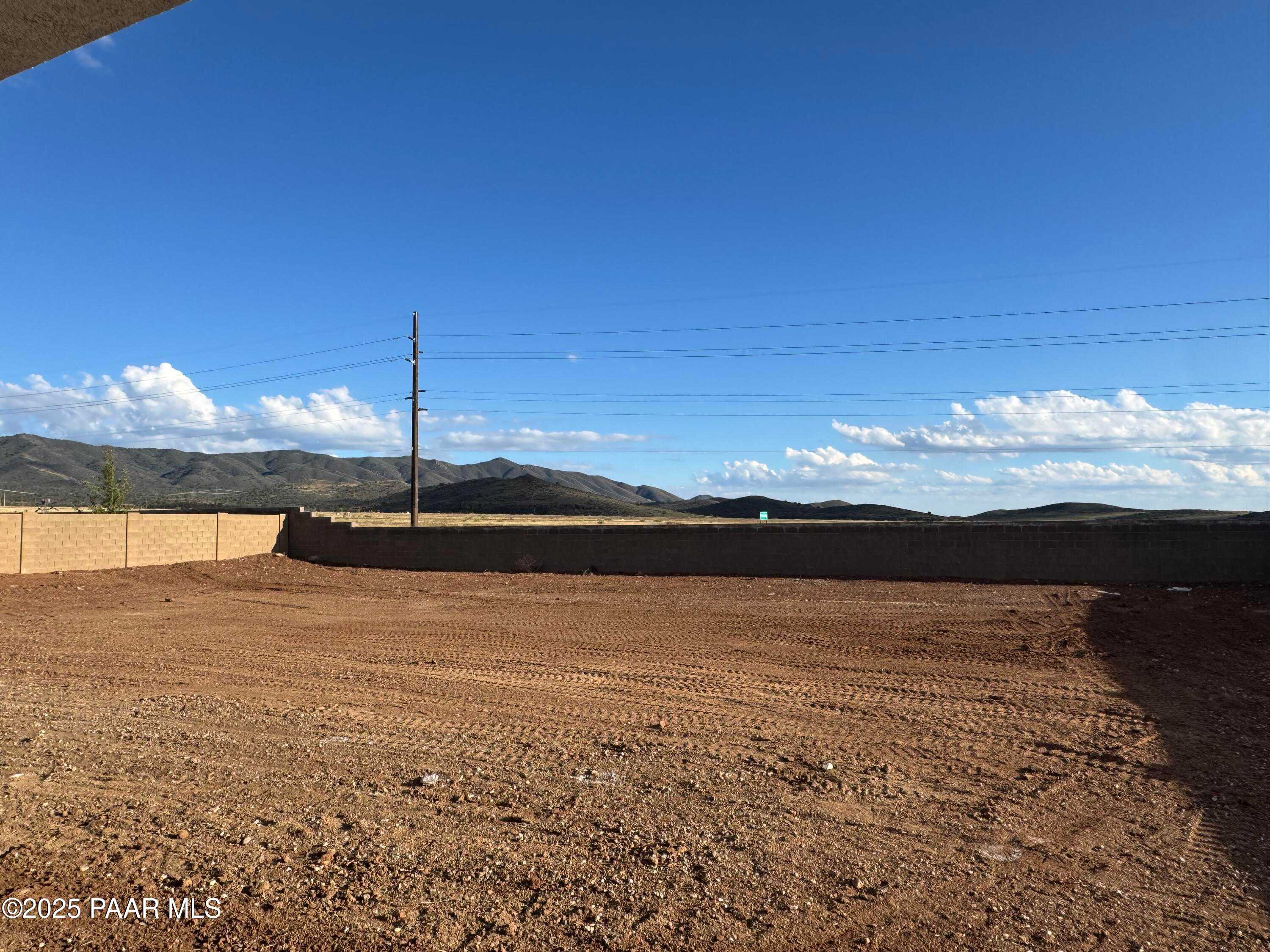 Graded dirt backyard lot with tan block fence, distant mountains, and utility pole under clear skies in Morningstar, Prescott Valley