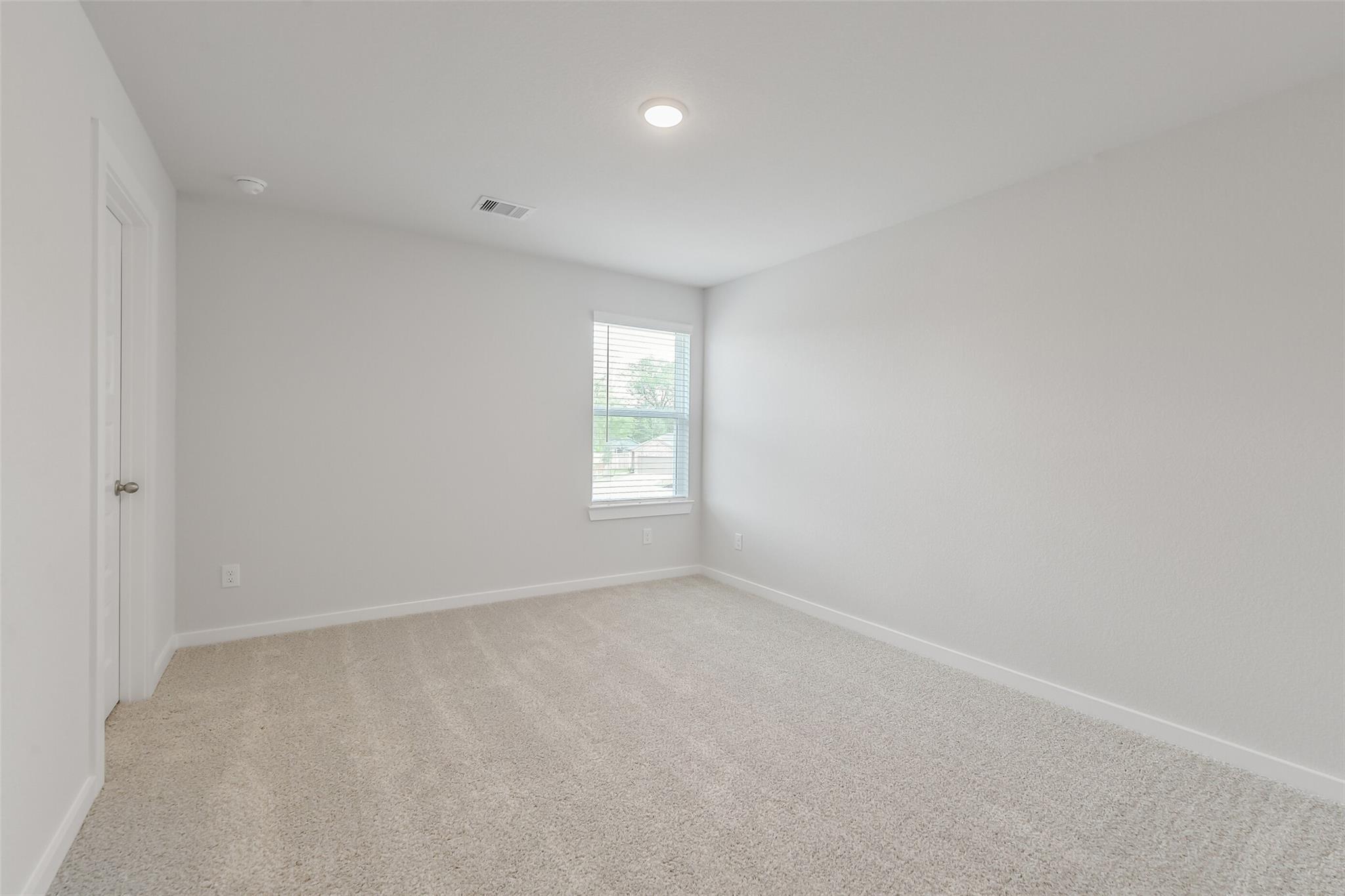 Spacious empty bedroom with light gray walls, beige carpet, window blinds, and recessed lighting in Davidson Homes San Marcos E, Conroe, Texas