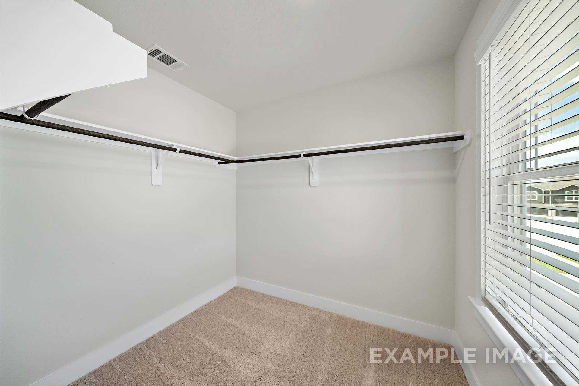Spacious walk-in closet in The Lily A master suite featuring built-in wooden shelves, hanging rods, beige carpet, and window blinds