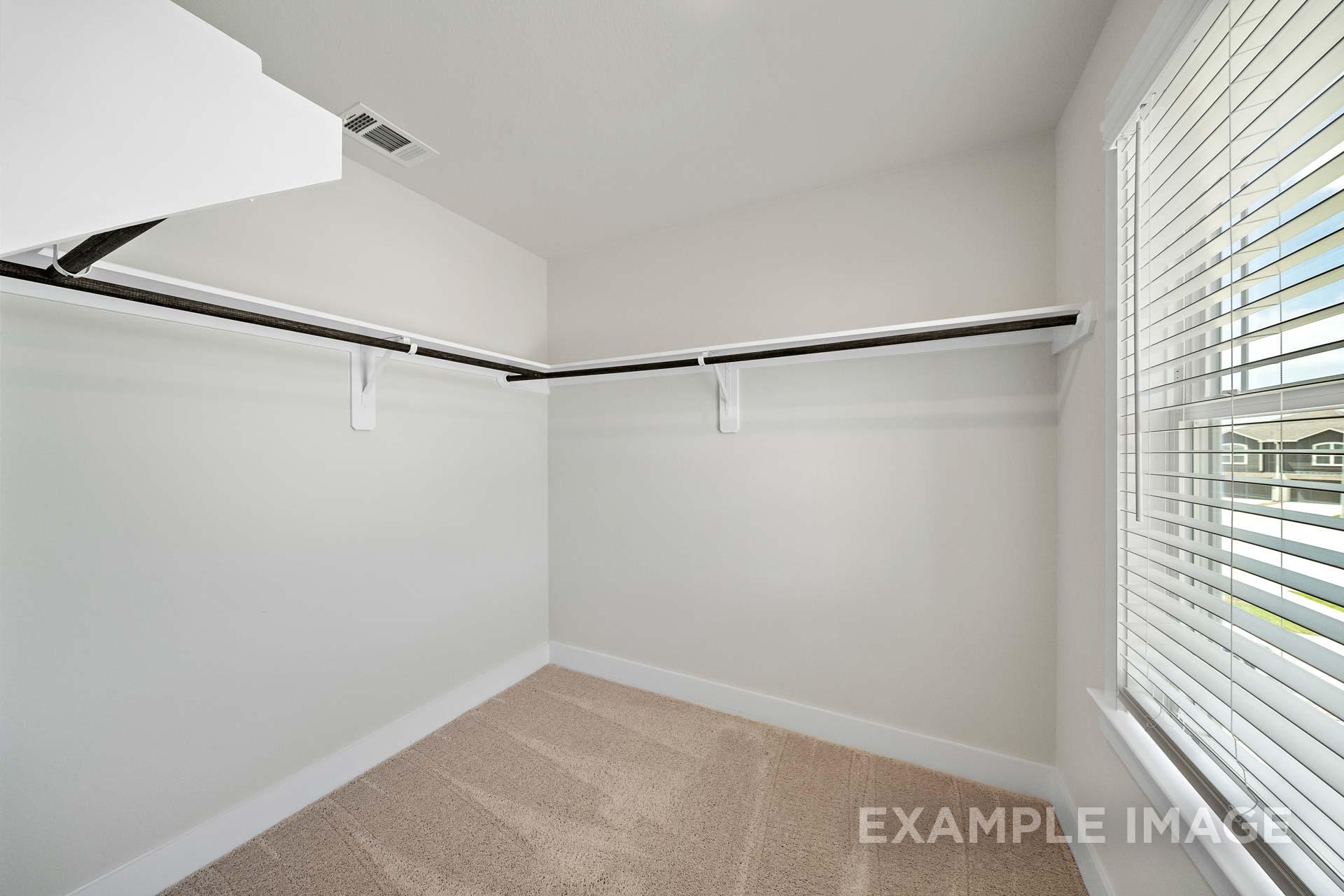Spacious walk-in closet in The Lily A master suite featuring built-in wooden shelves, hanging rods, beige carpet, and window blinds