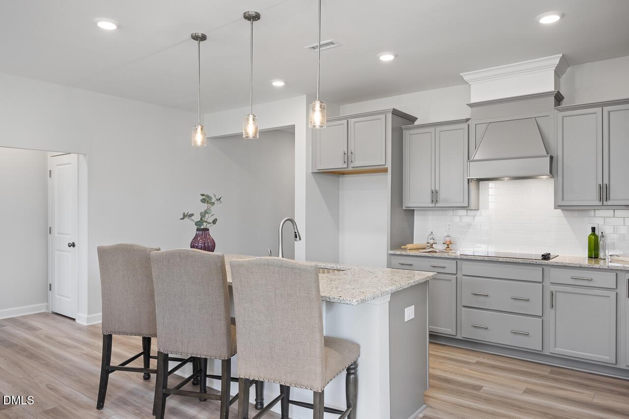 Modern gray shaker kitchen with quartz island, subway tile backsplash, and pendant lights in Davidson Homes The Daphne D, Zebulon NC