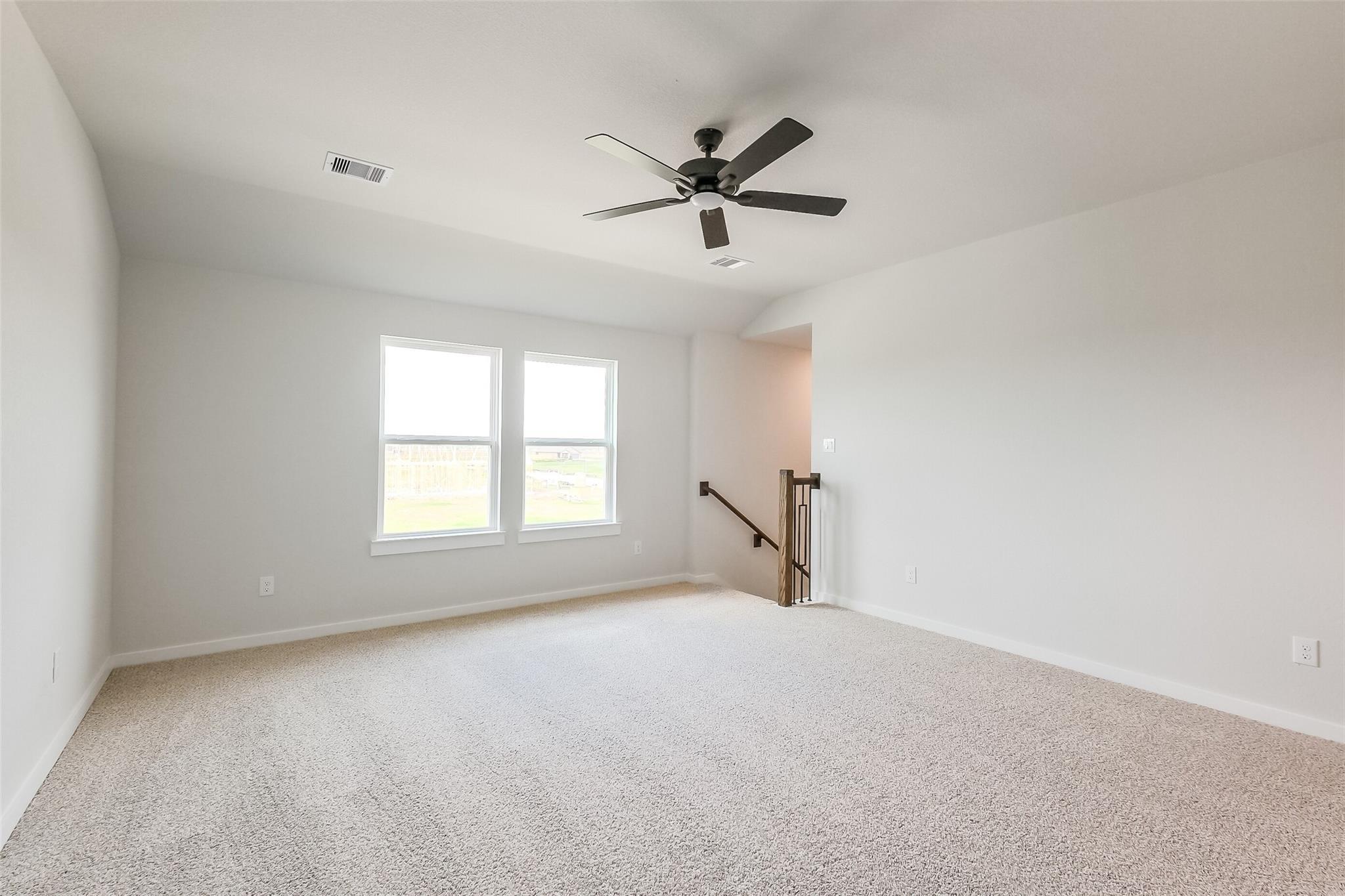 Bright upstairs loft with large windows, ceiling fan, and carpeted flooring in Davidson Homes The Tierra B, Beasley, Texas