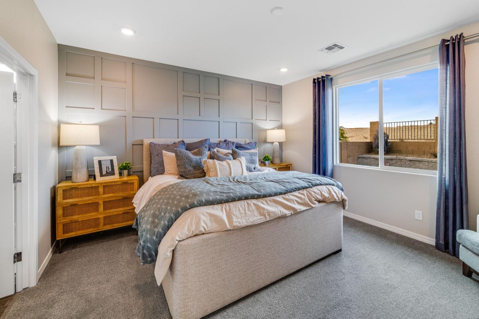 Spacious master bedroom in The Newport with king bed, neutral paneled walls, wooden nightstands, and large window view