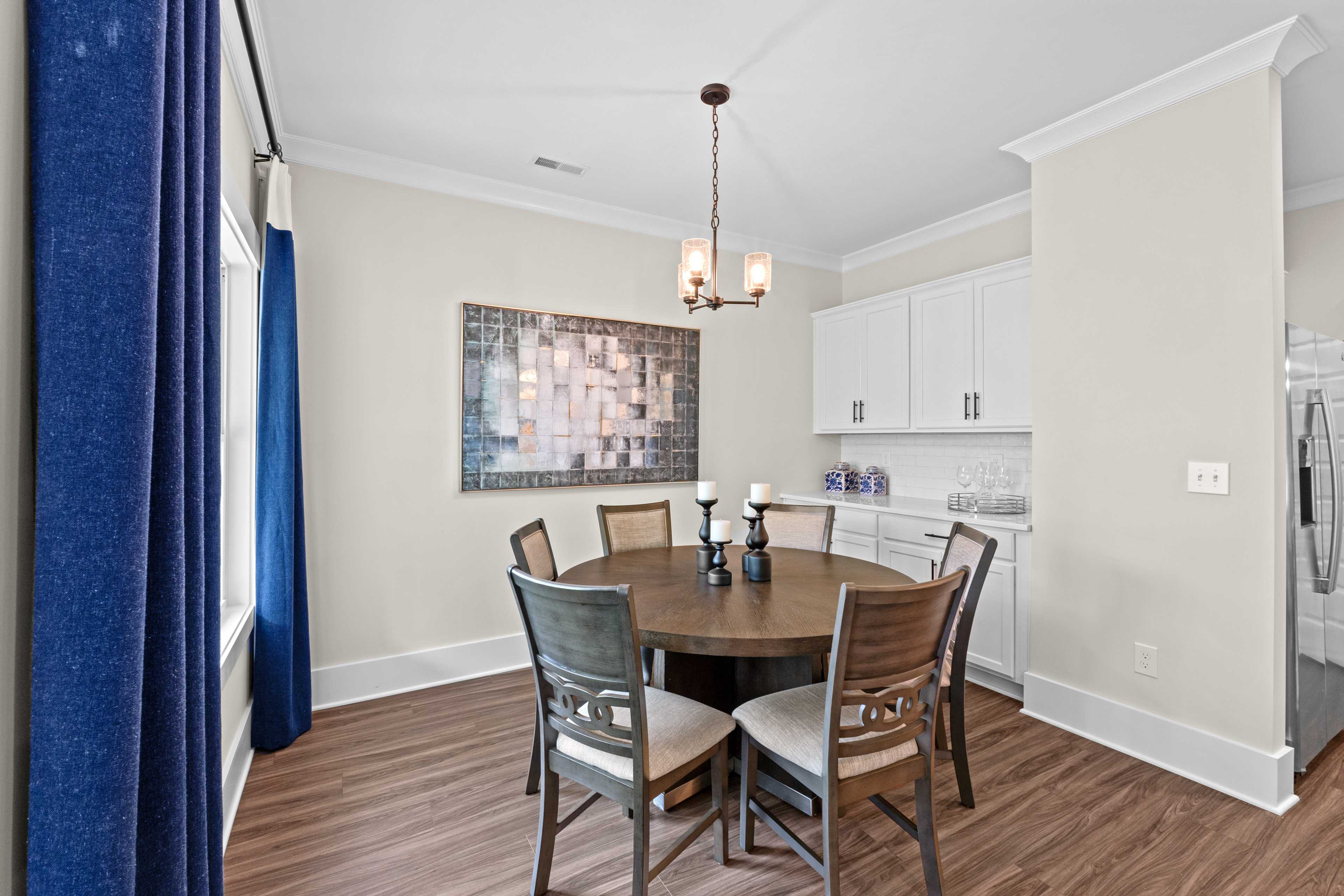 Spacious dining room at Ivy Hills in Toney Alabama with round wooden table, chandelier, blue curtains, and open kitchen by Davidson Homes