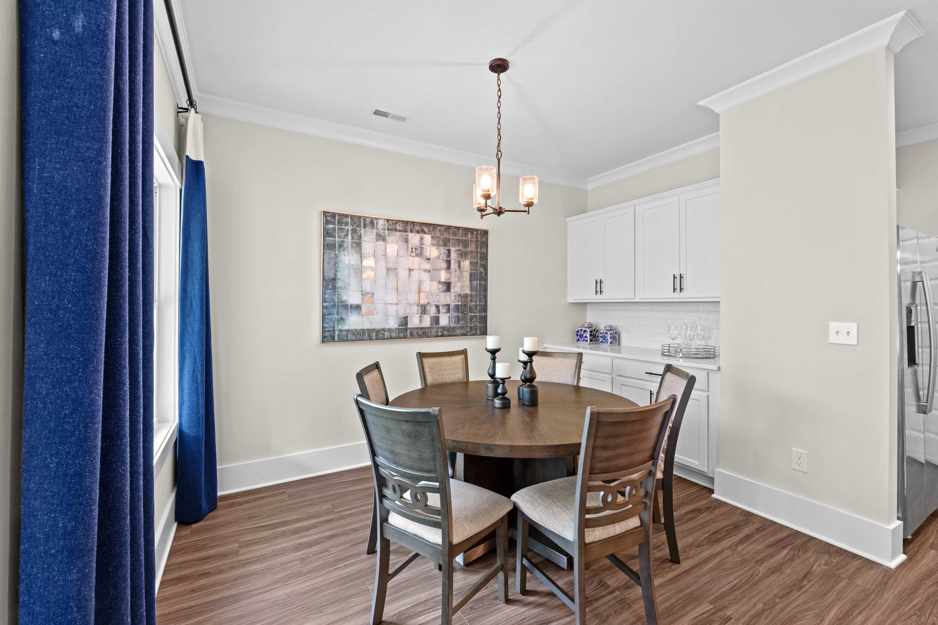 Spacious dining room at Ivy Hills in Toney Alabama with round wooden table, chandelier, blue curtains, and open kitchen by Davidson Homes